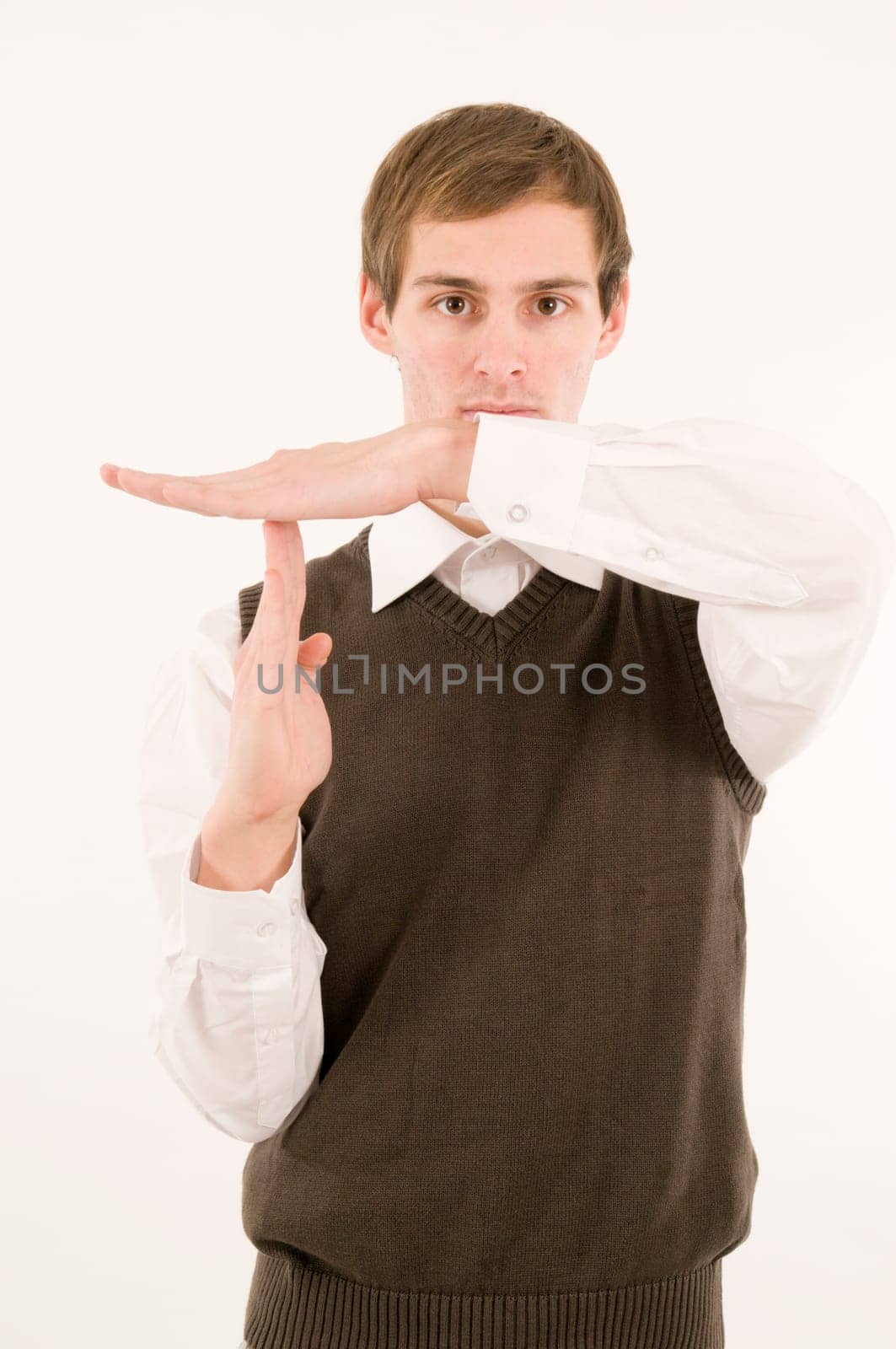 Frontal upper body view of young man in white shirt and brown vestover showing time-out hand signal to camera against white background