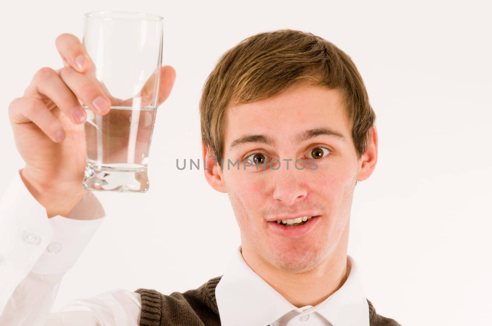 Frontal head and shoulders shot of young man with raised glass of water against white background and looking at camera