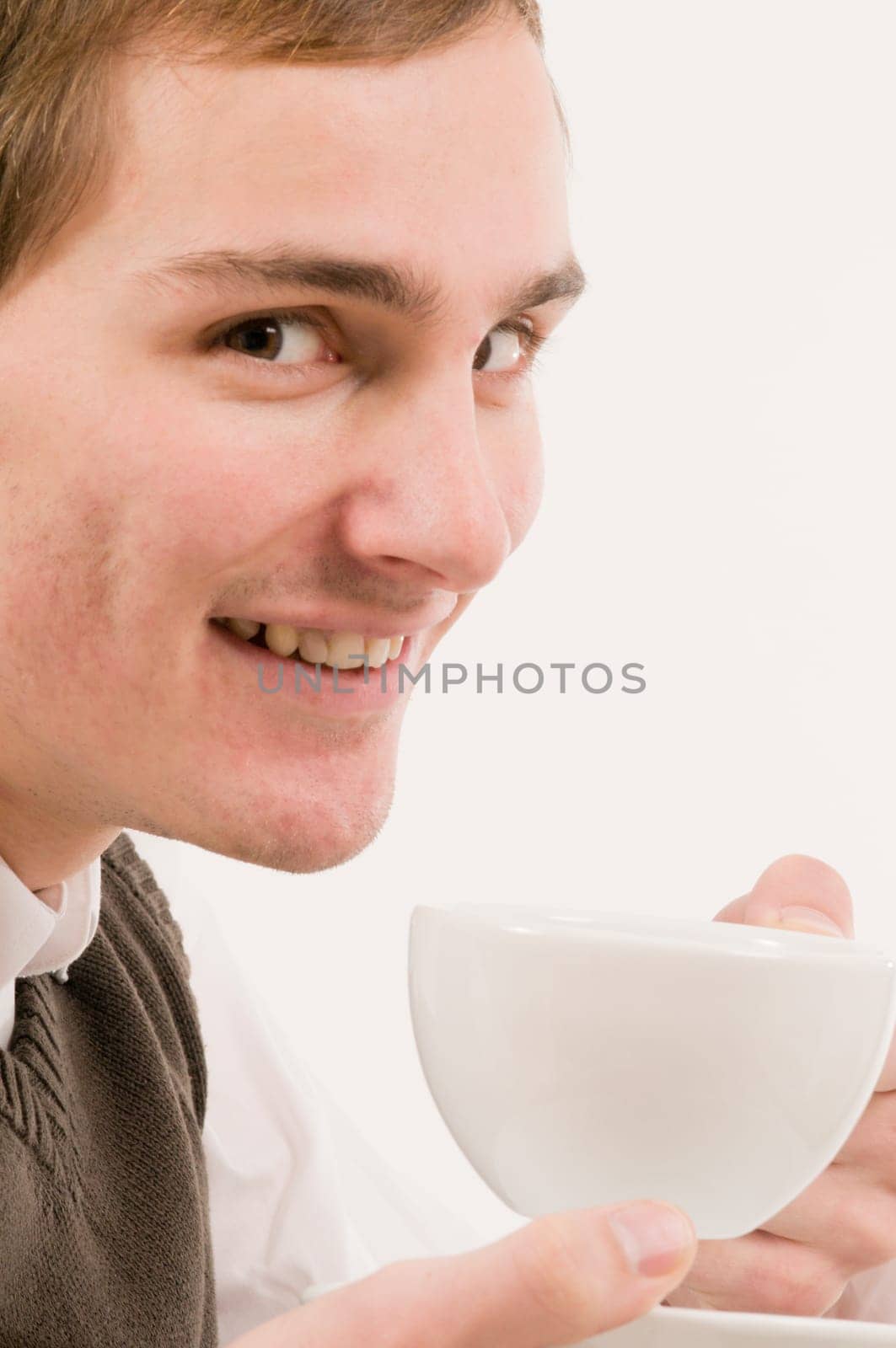 Side head and shoulders shot of young man looking happily at camera holding white cup against white background