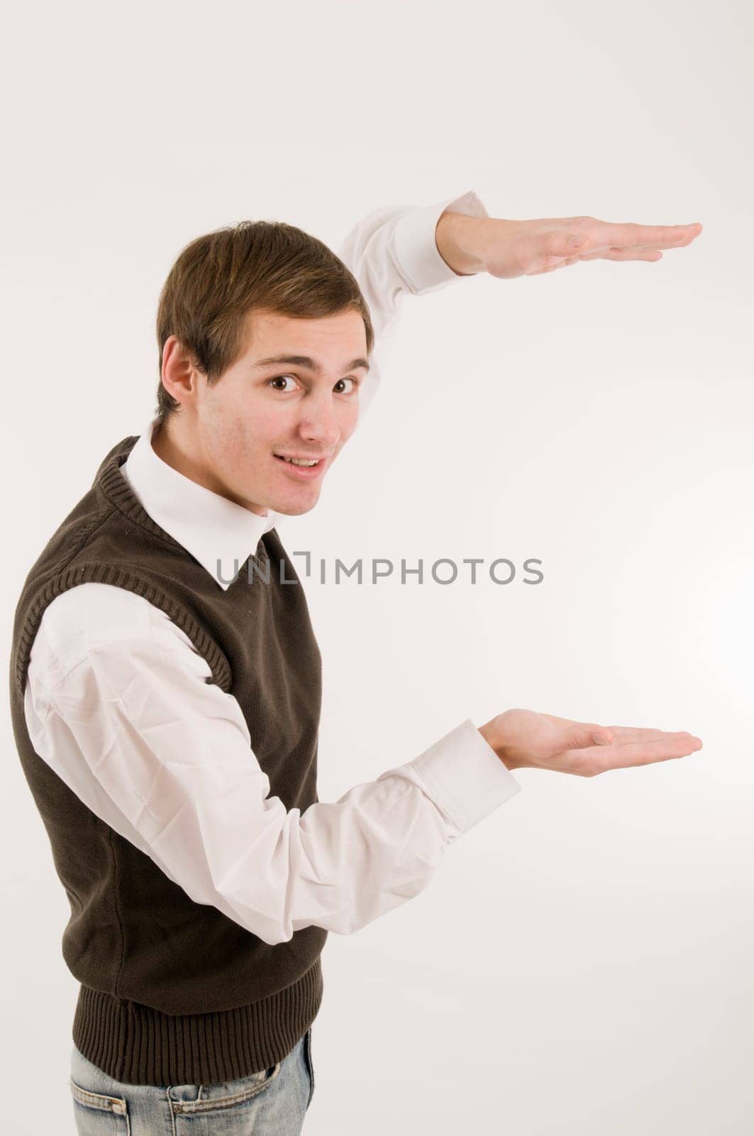 Side torso shot of a young man in jeans,white shirt and brown vestover,holding a virtual non-existent cardboard box against a white background and looking at the camera with a smile