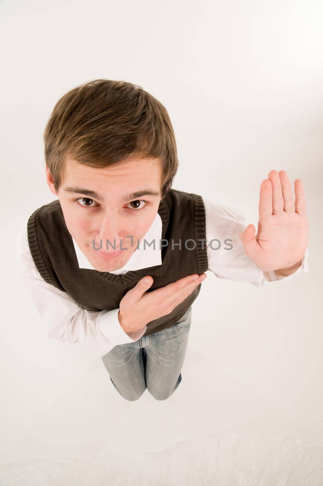 wide-angle top view of a young man in front of a white background in a white shirt and brown vestover,his hand raised in oath looking into the camera
