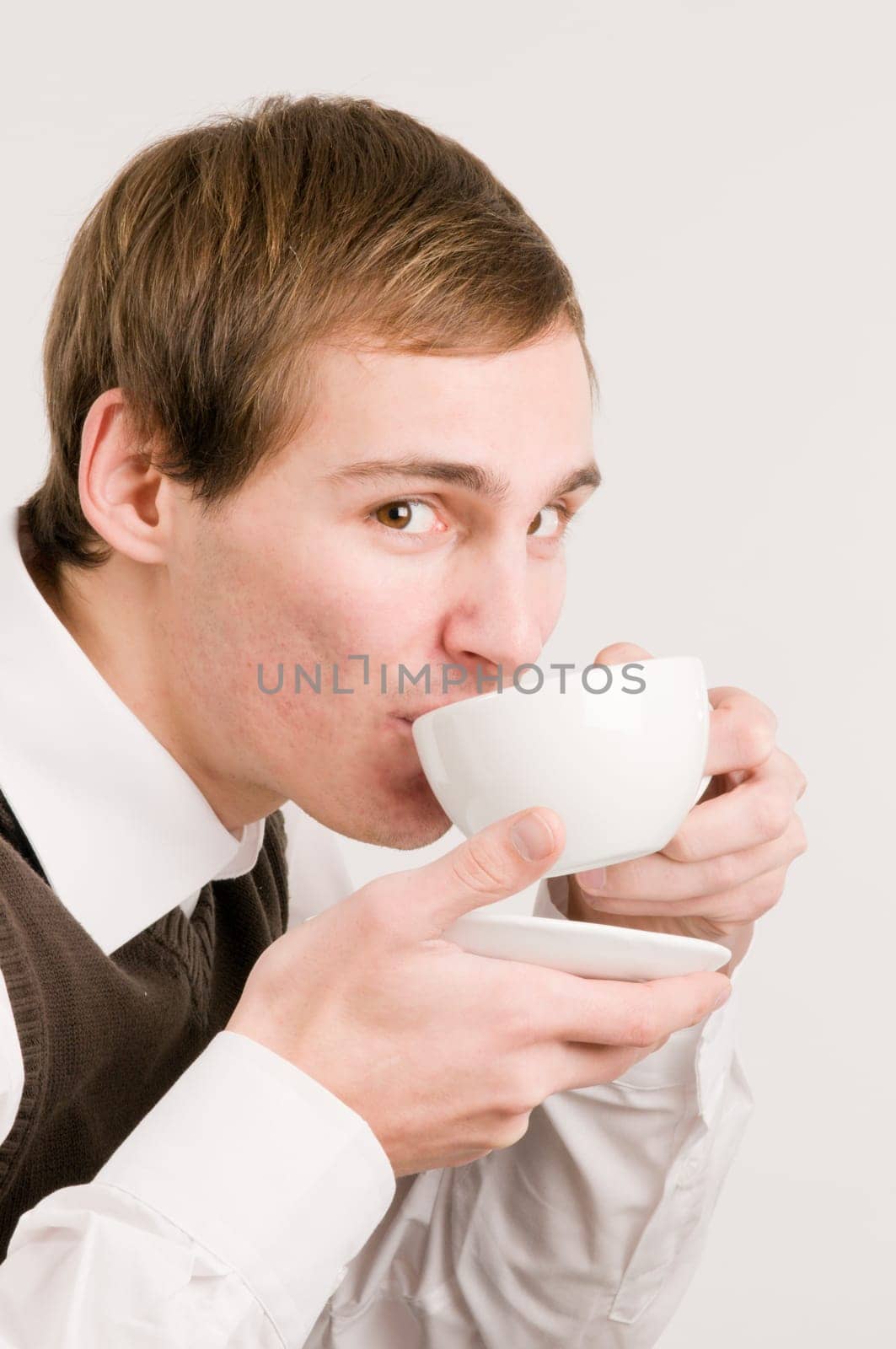 Side head and shoulders shot of a young man drinking from a white cup against a white background