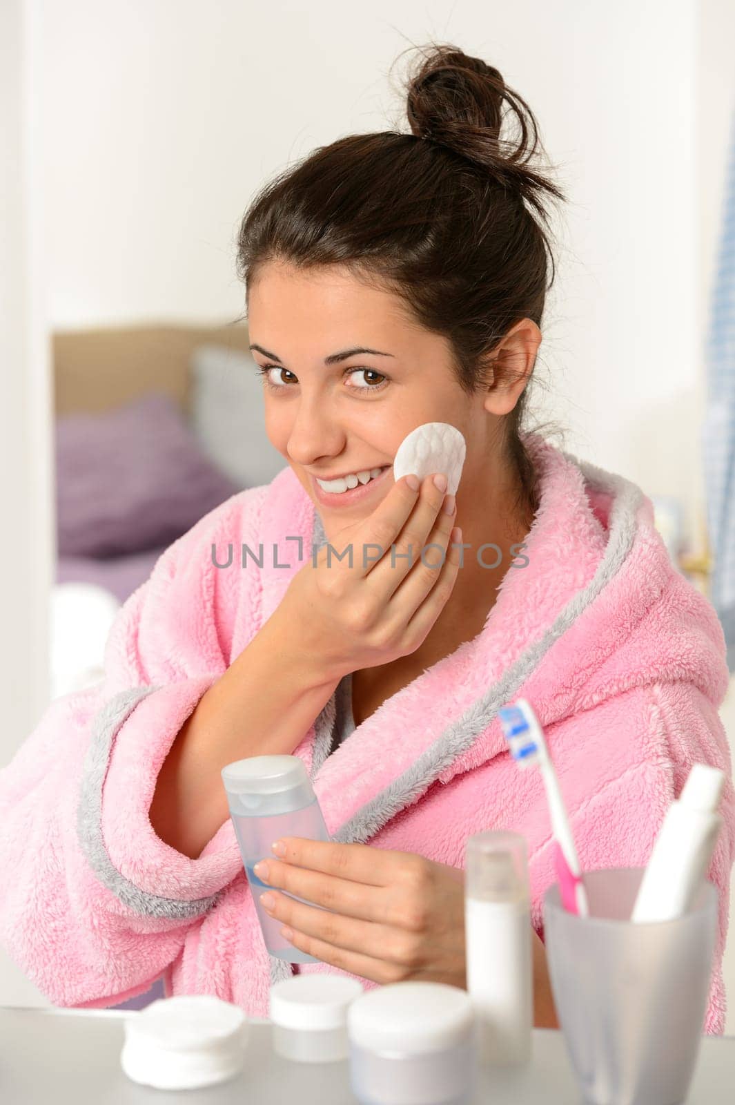 Young smiling woman cleaning face with cotton pad