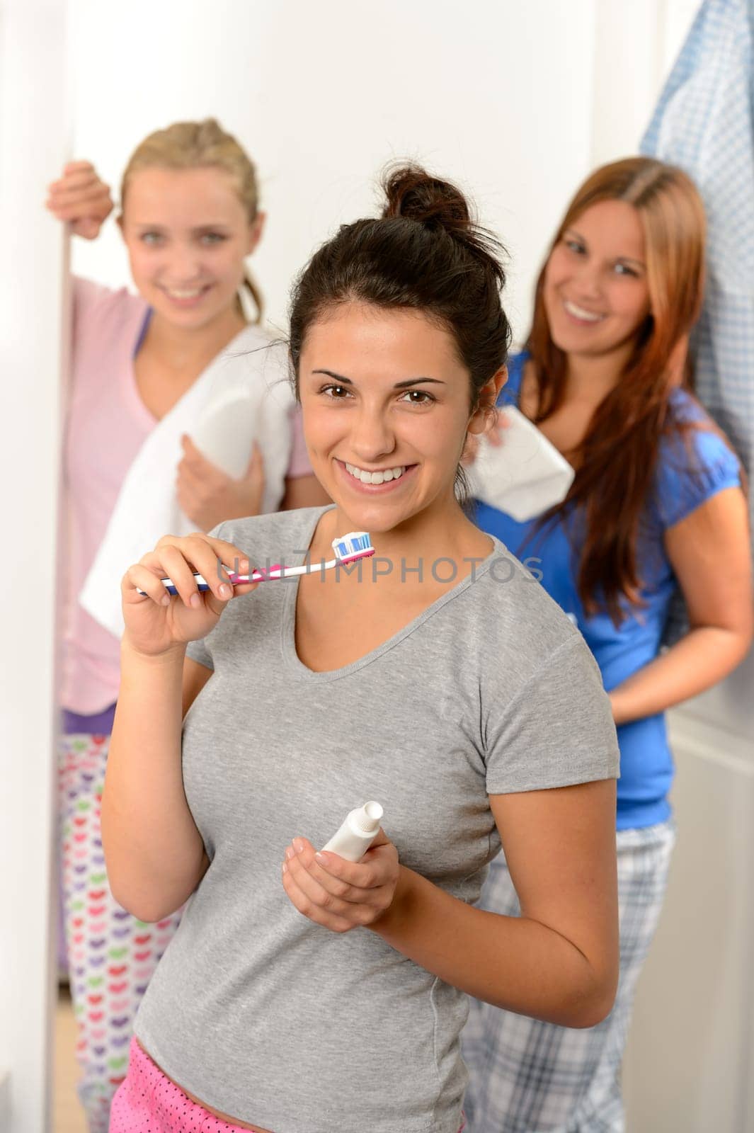 Teenage girl washing her teeth with friends in the bathroom