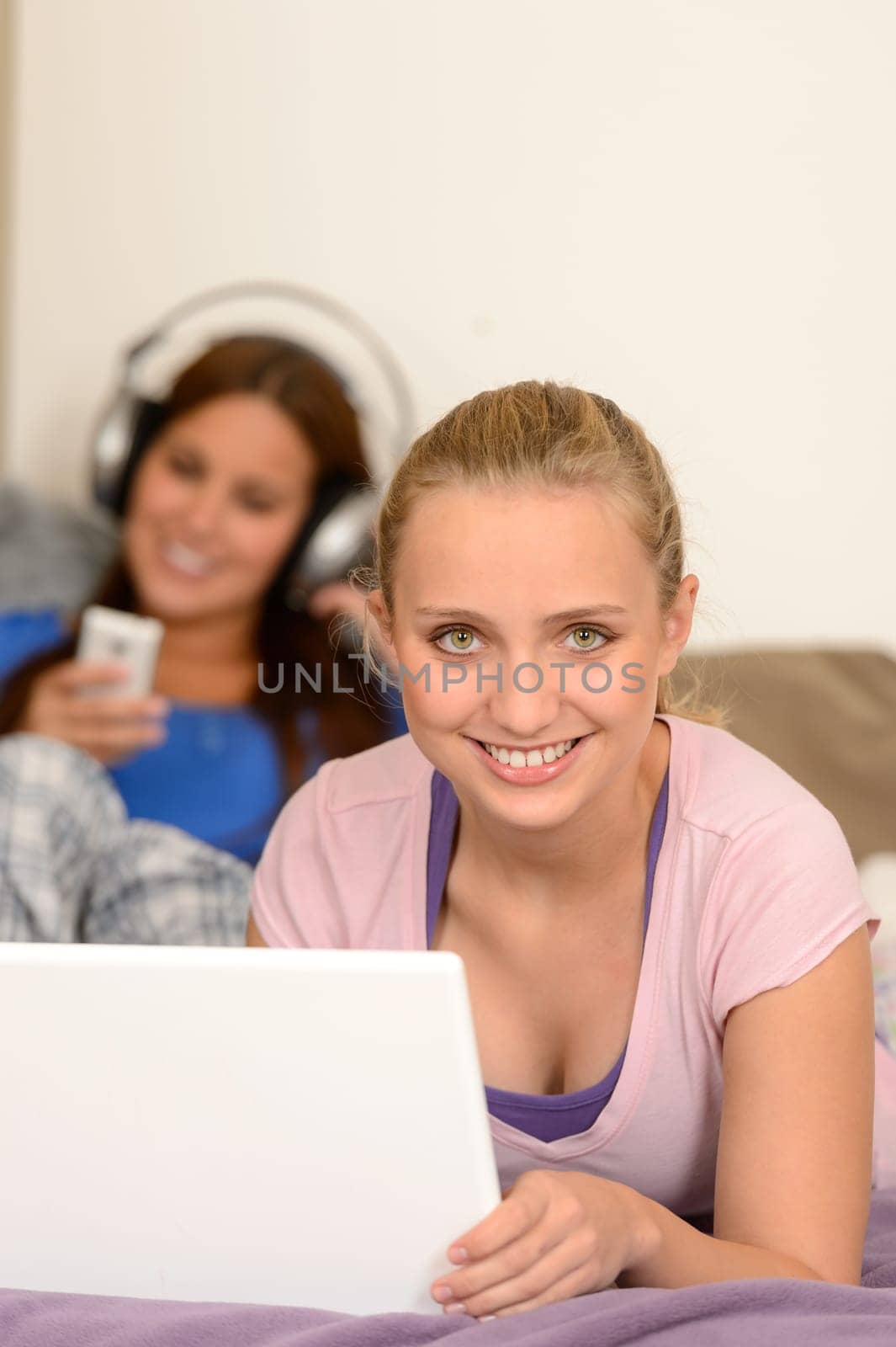 Smiling girls studying on laptop her sister listening music