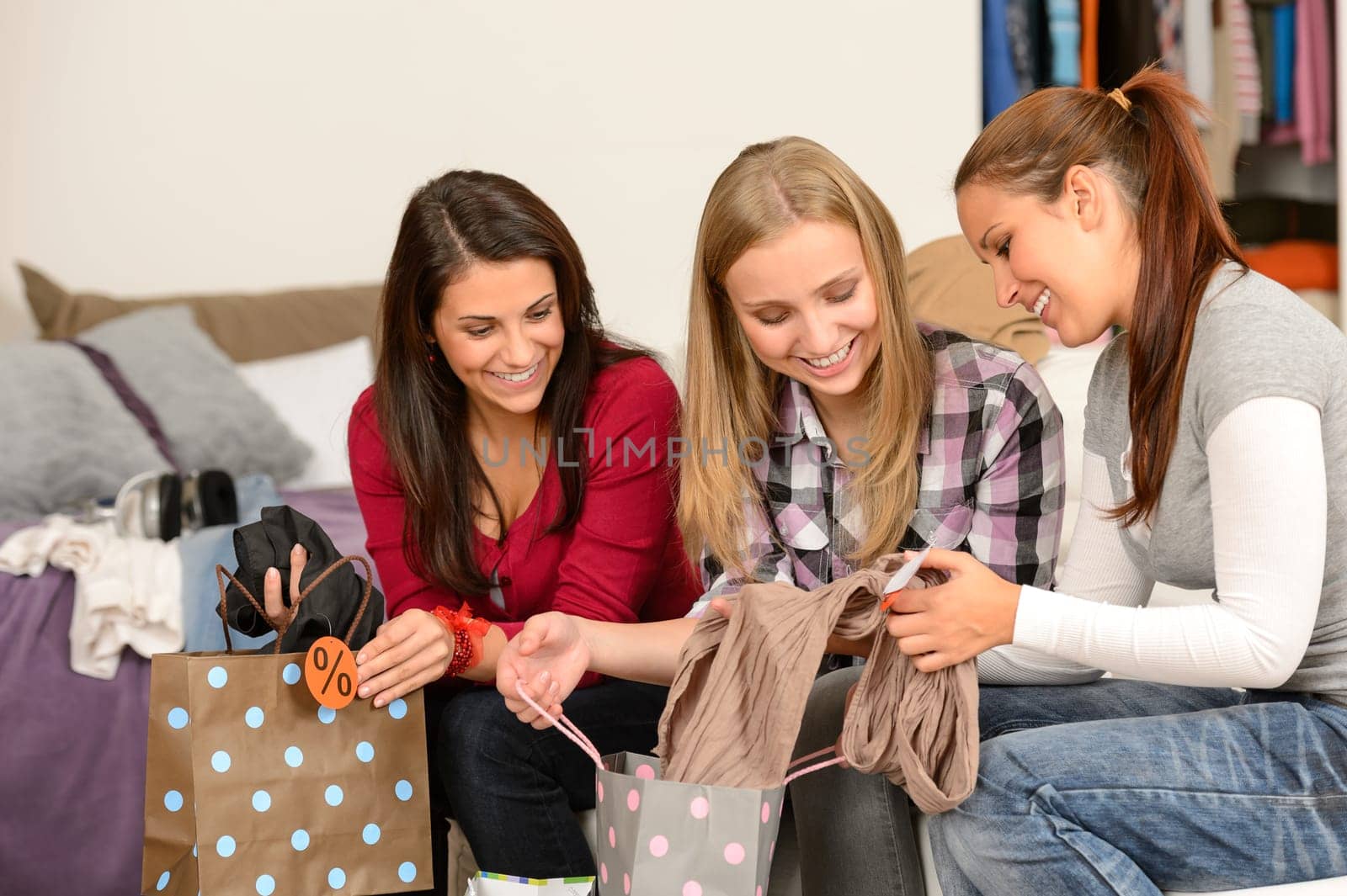 Three cheerful girls with clothes from sale shopping bags