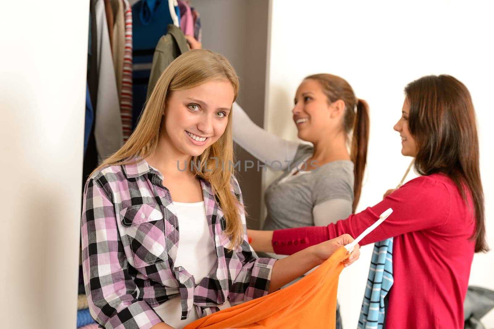 Happy teenagers friends choosing clothes from wardrobe