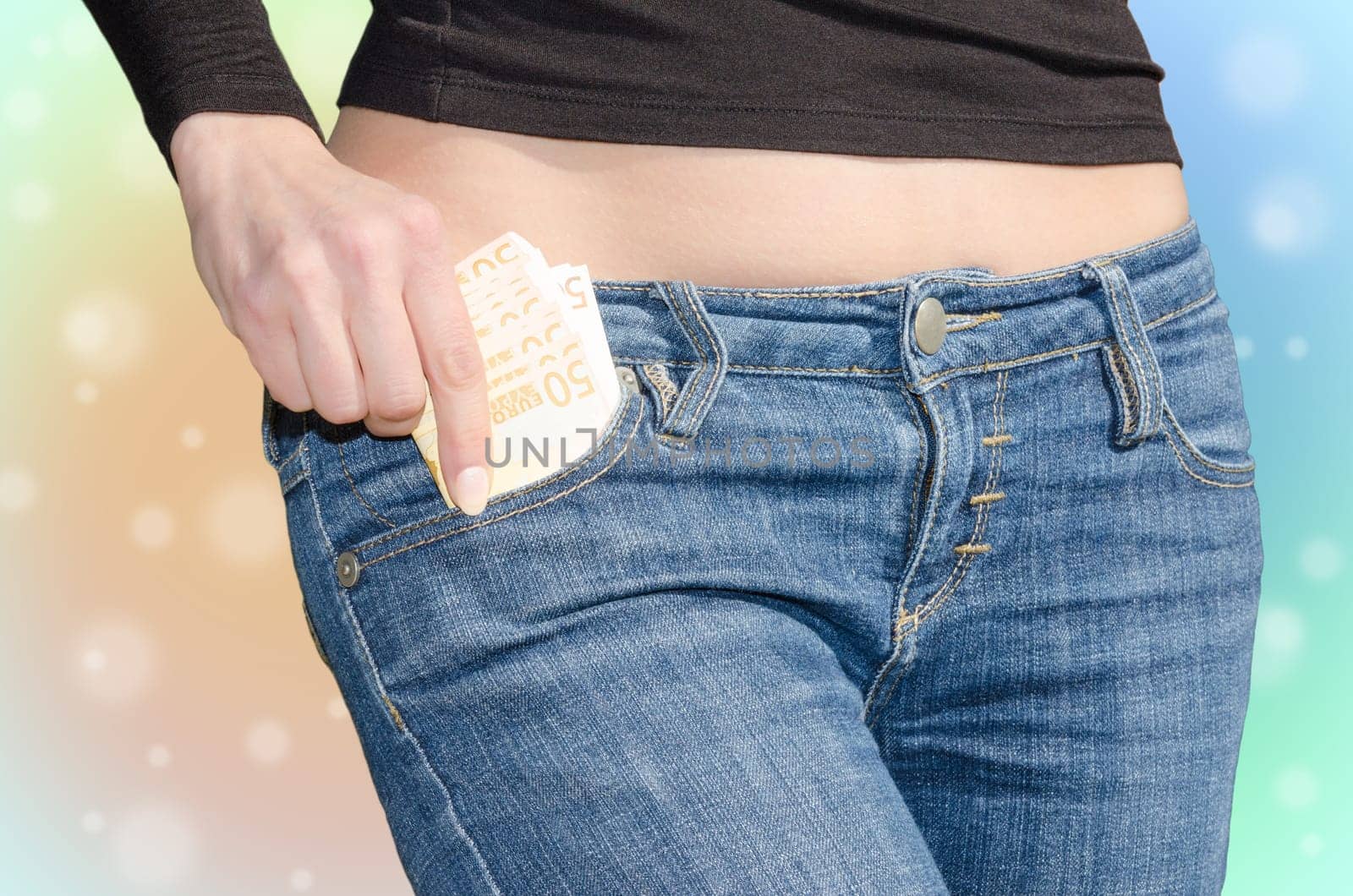 Young woman with naked tummy puts money in your jeans pocket on colored background
