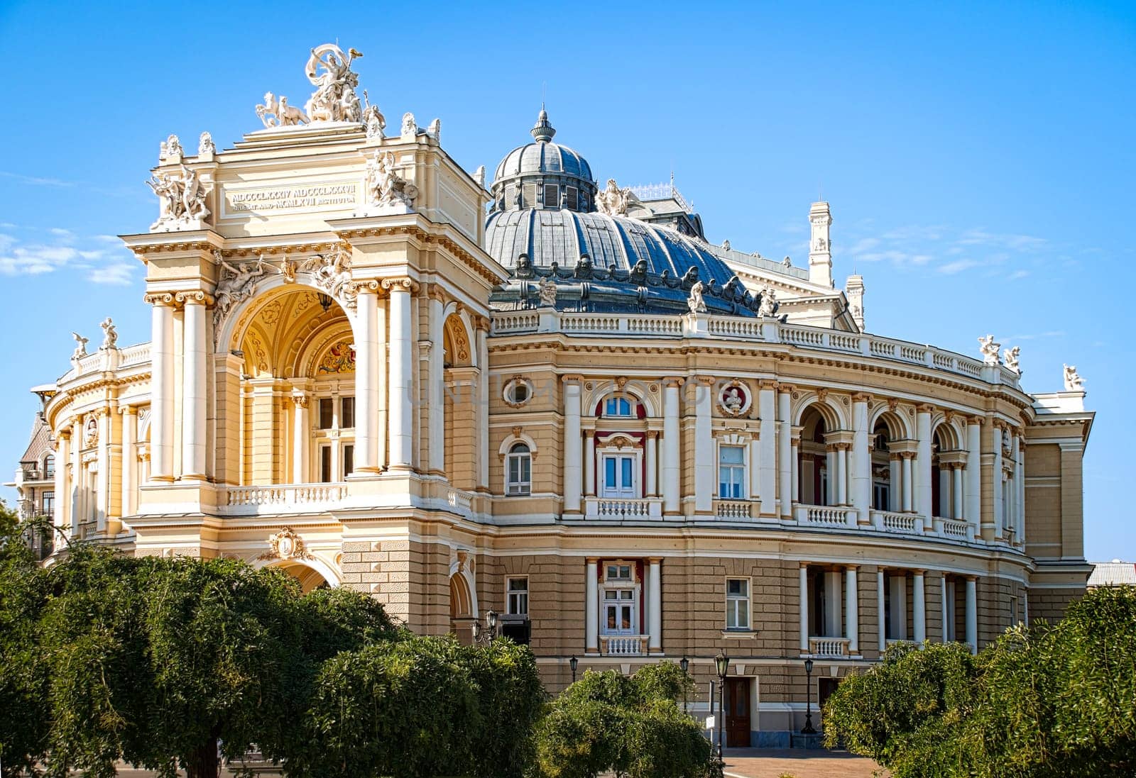 Odesa opera theatre with blue sky in background and trees in foreground (Odesa or Odessa, Ukraine)