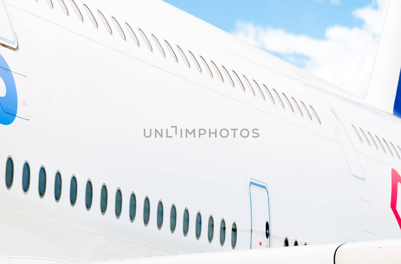 Side view of white passenger plane with two rows of windows and blue cloudy sky in background. Place for copy.
