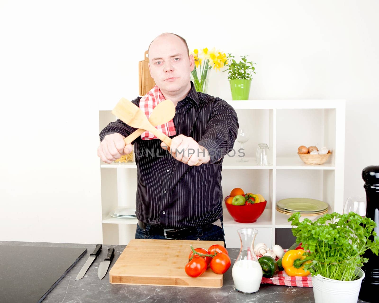 Fun image of a man preparing to start cooking a healthy vegetarian meal standing holding up the wooden salad utensils crossed in front of him with a look of determination