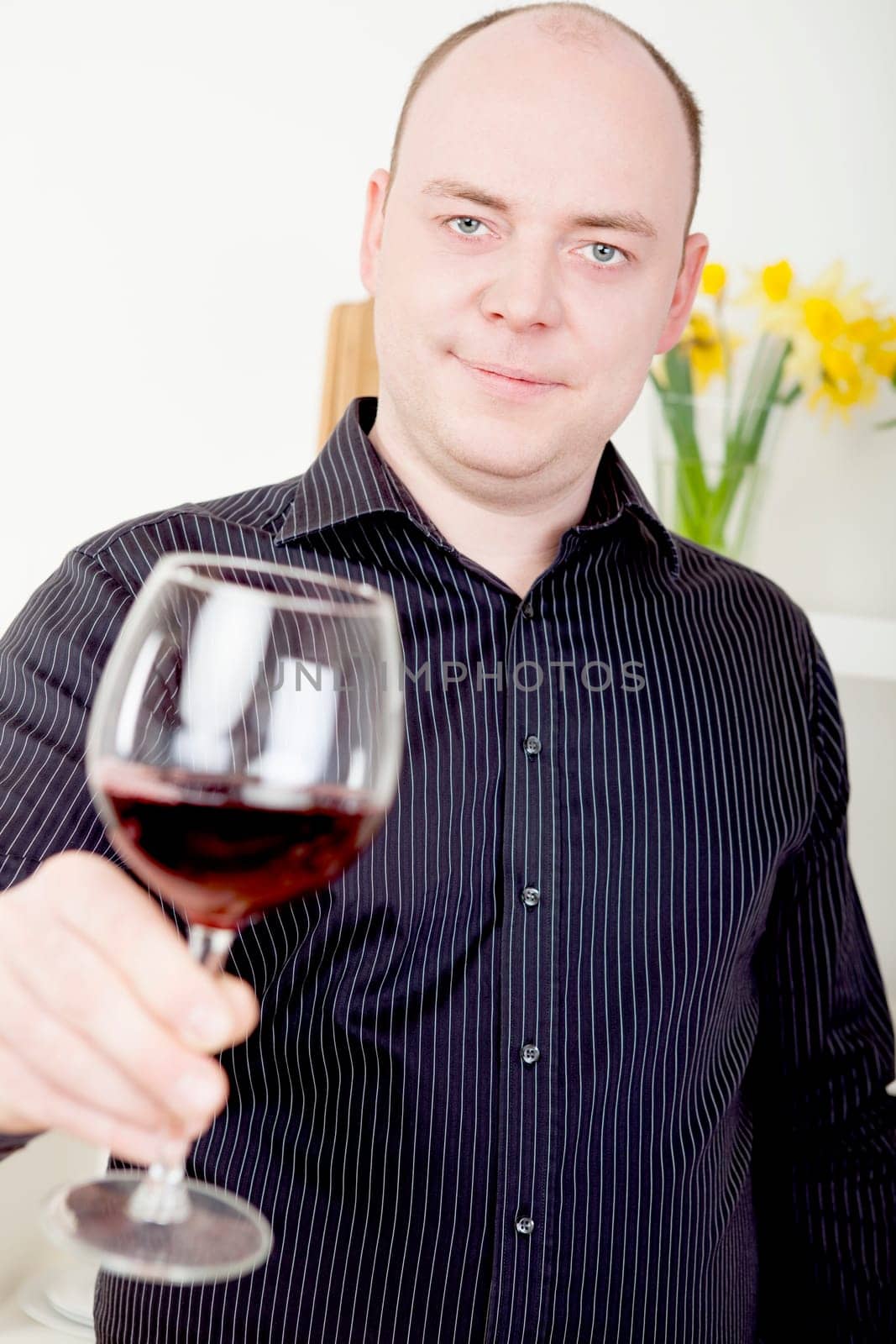 Attractive mature man raising his glass to the camera in a toast of celebration , as an acknowledgement or in a polite greeting