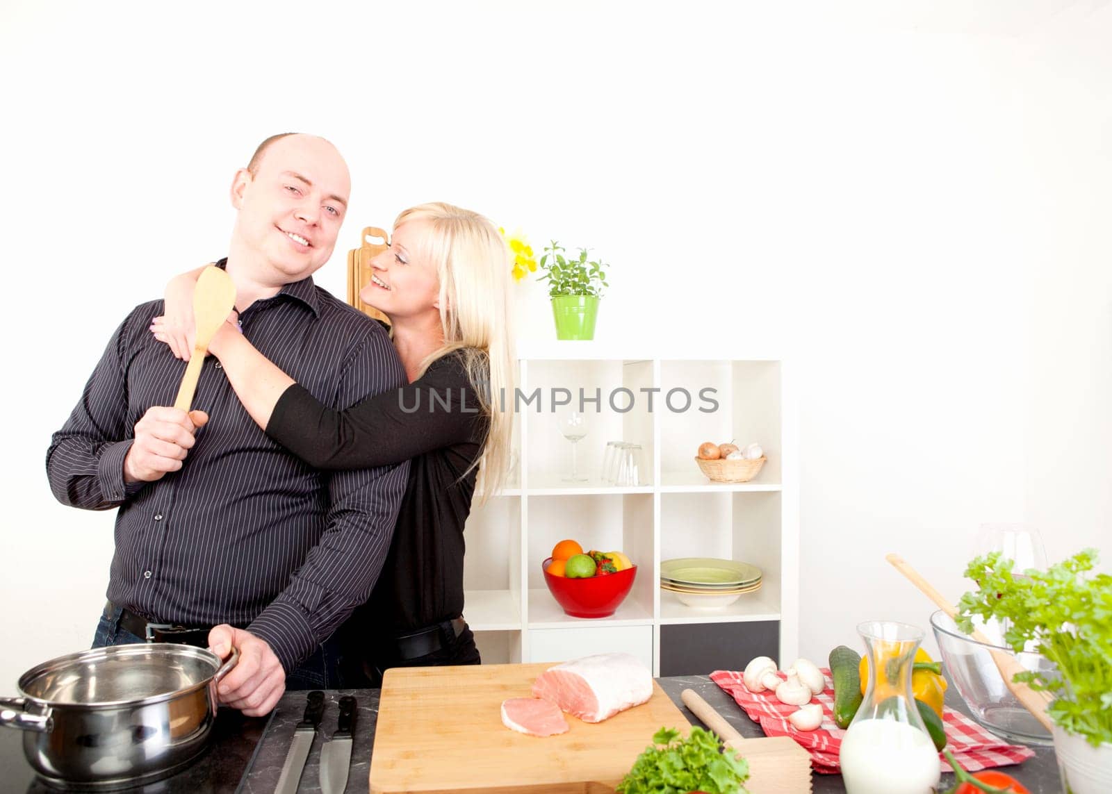 Romantic happy couple enjoying an affectionate embrace stand in the kitchen preparing a meal from an array of fresh healthy ingredients