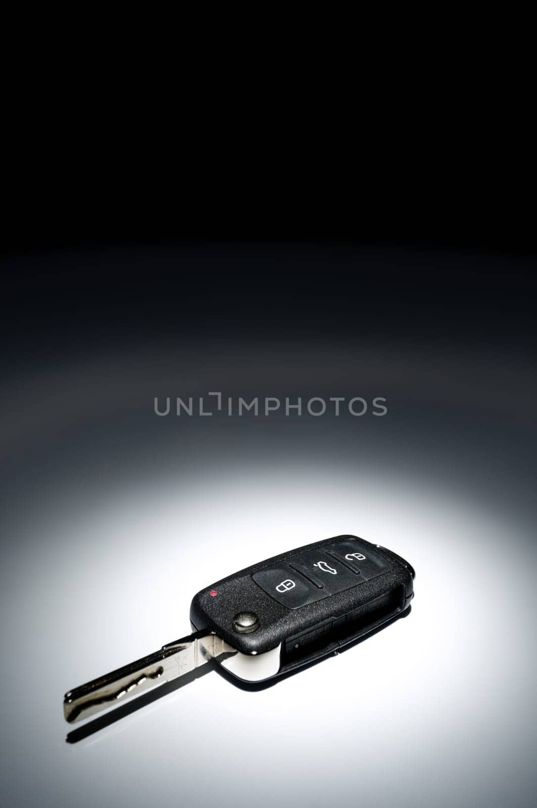 Modern black open car key on dark background in spot of light, wide angle, horizontal.
