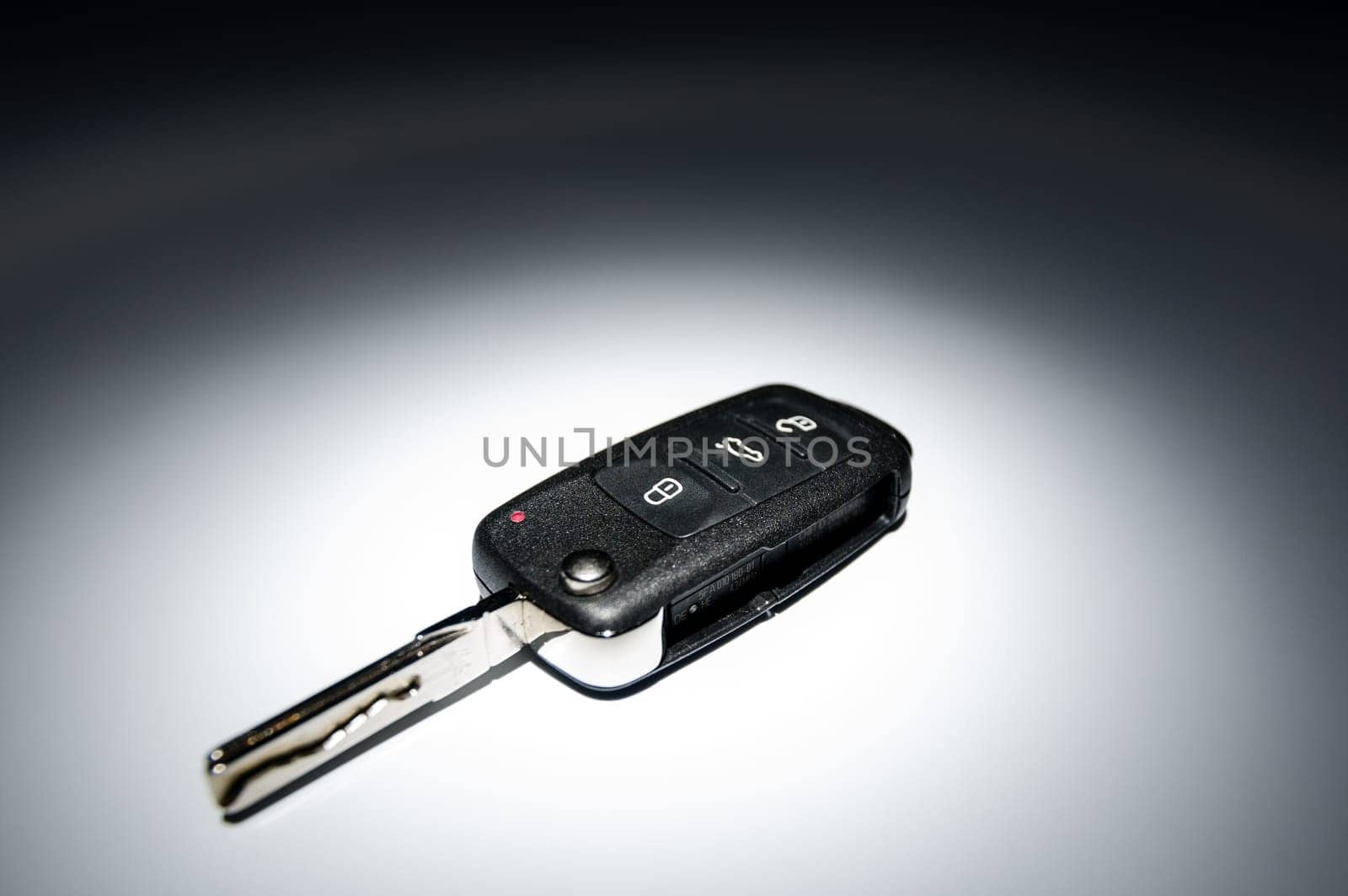 Modern black open car key on dark background in spot of light, wide angle, horizontal.