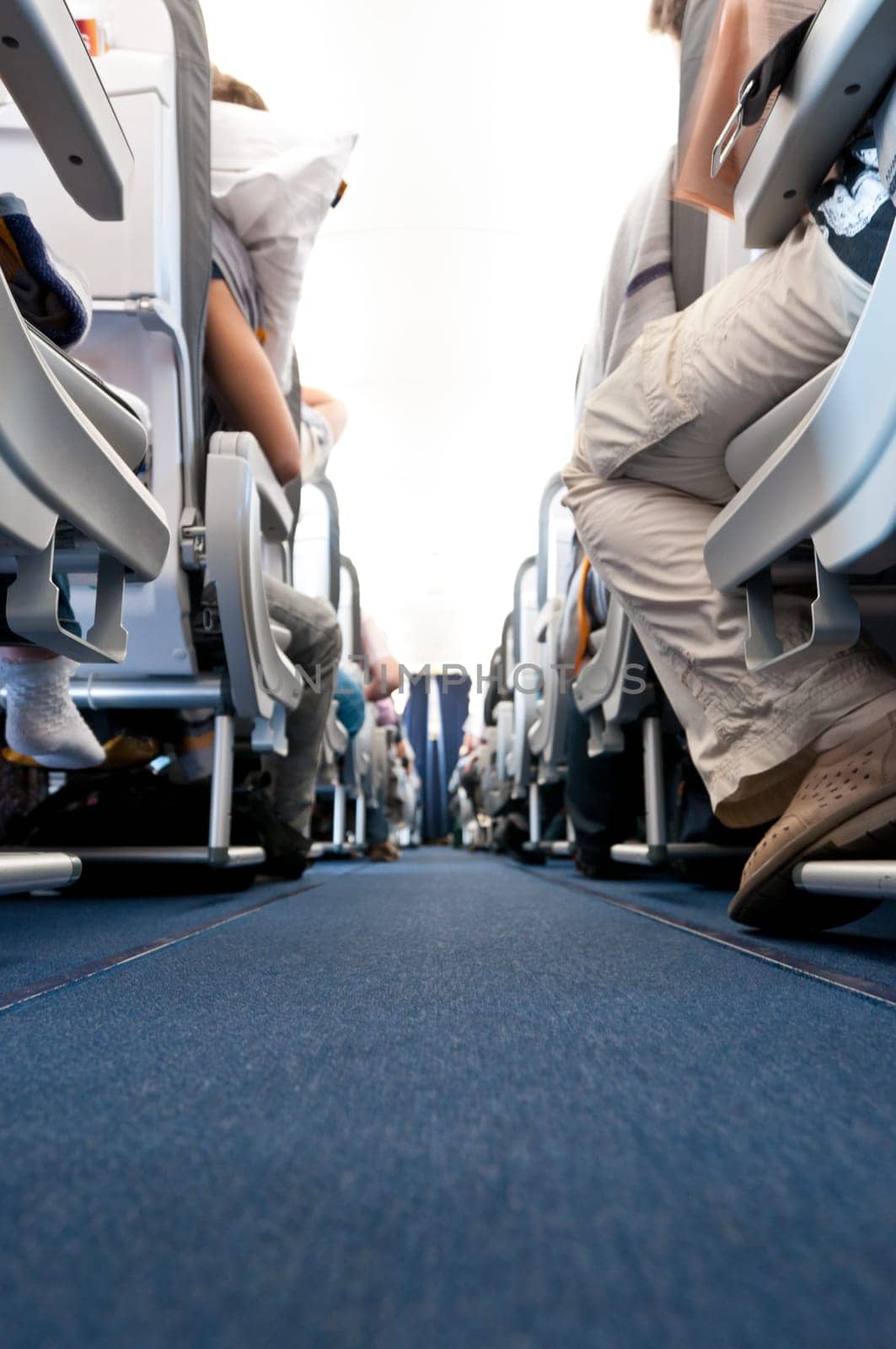 Low angle view of air plane cabin aisle with rows of seats by the sides. People on seats, none recognizable.
