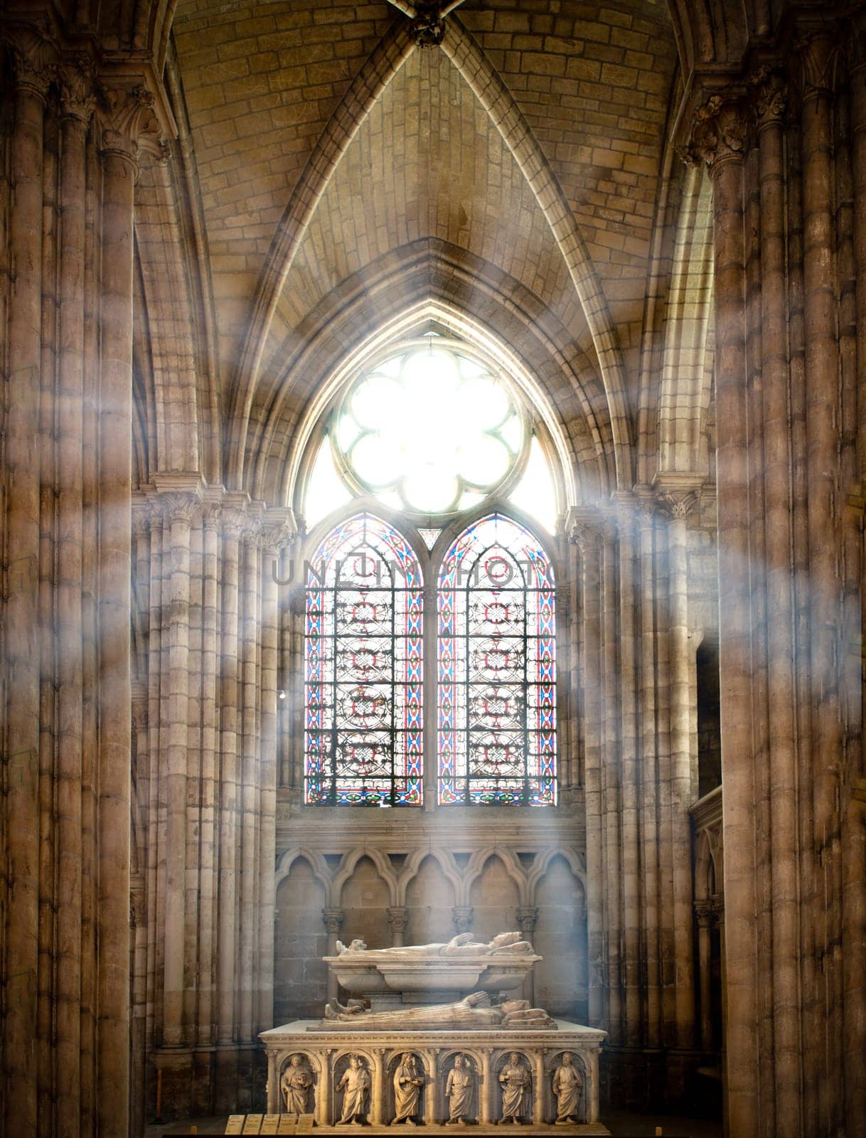 sun rays beaming through the old stained glass window of saint denis cathedral and lighting interior with tomb. Paris, France, Europe.