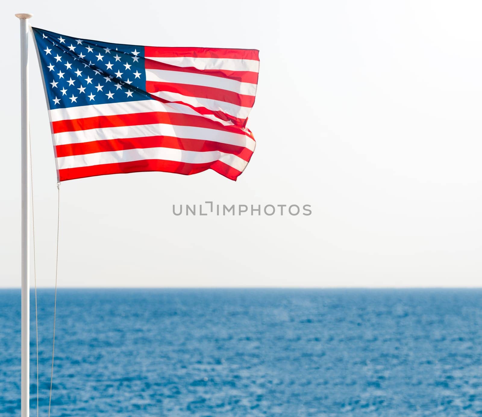 united states of america flag on pole with blue sea in background and clear sky. Lots of copy space.