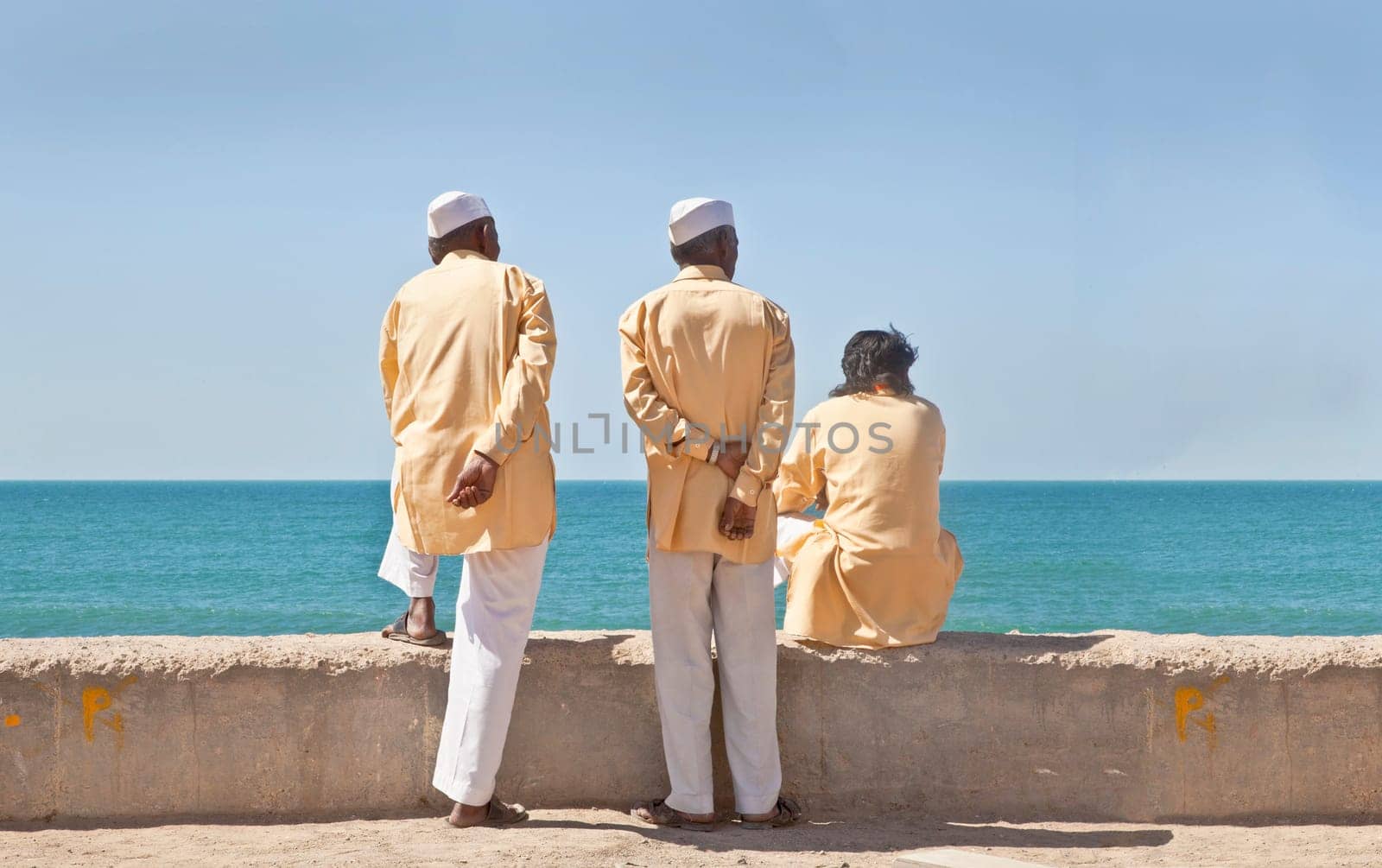 Horizontal portrait of three clerics in formal attire looking  out to the horizon of the Arabian Sea. The location of this conceptual shot was at the beach and promenade at Dwarka, Gujarat, India near the Krishna Temple.