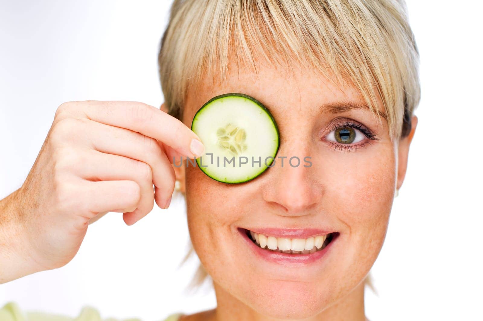young blond woman holding cucumber on face close up