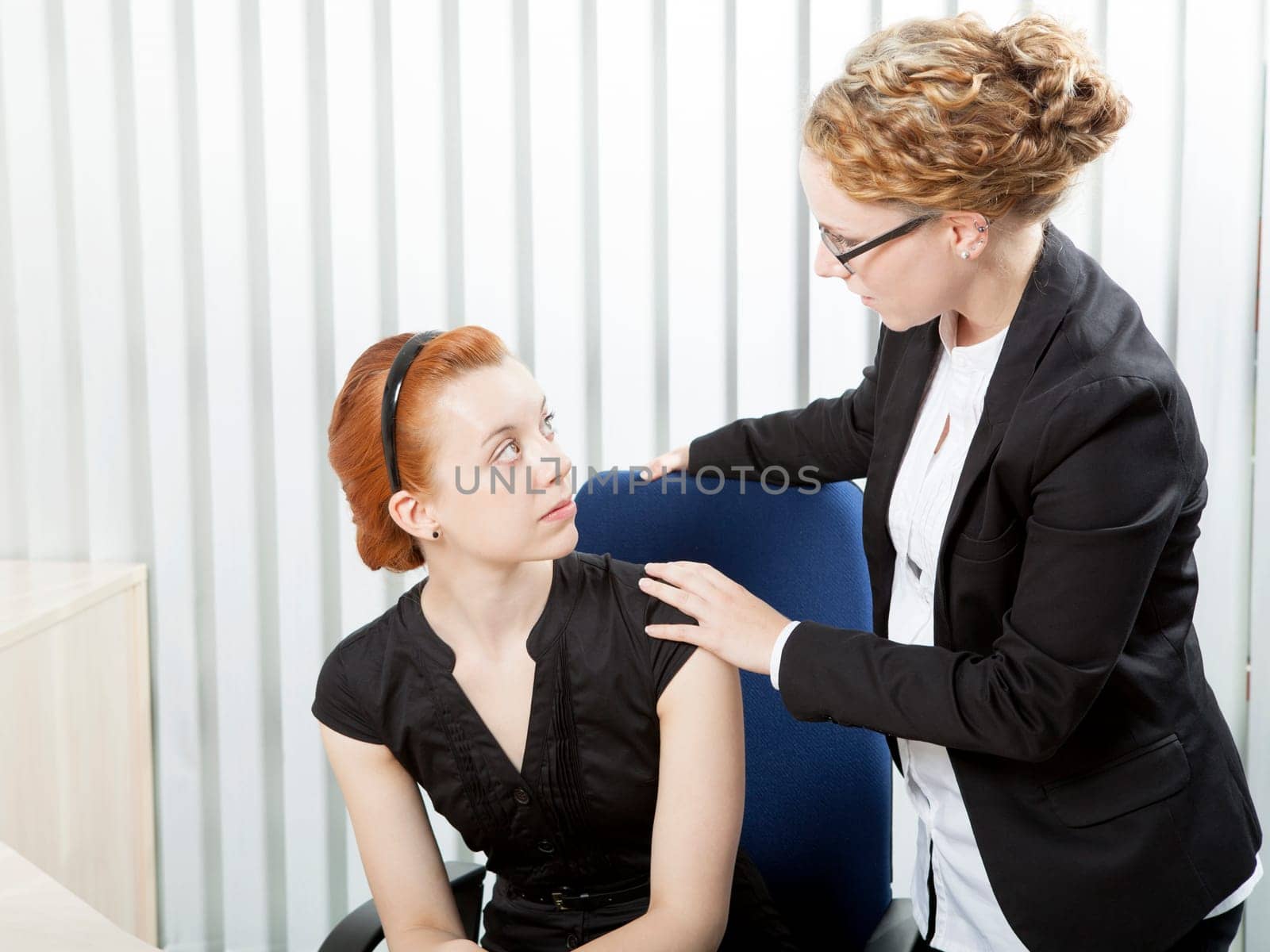 Female corporate supervisor talking to an employee laying a comforting hand on her shoulder as she tells her she is about to be made redundant