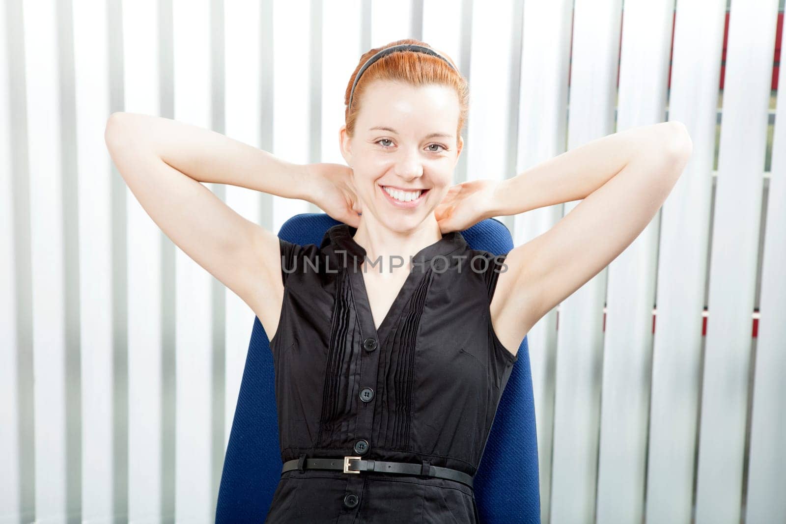 Smiling successful businesswoman leaning back in her chair with her hands behind her neck beaming at the camera