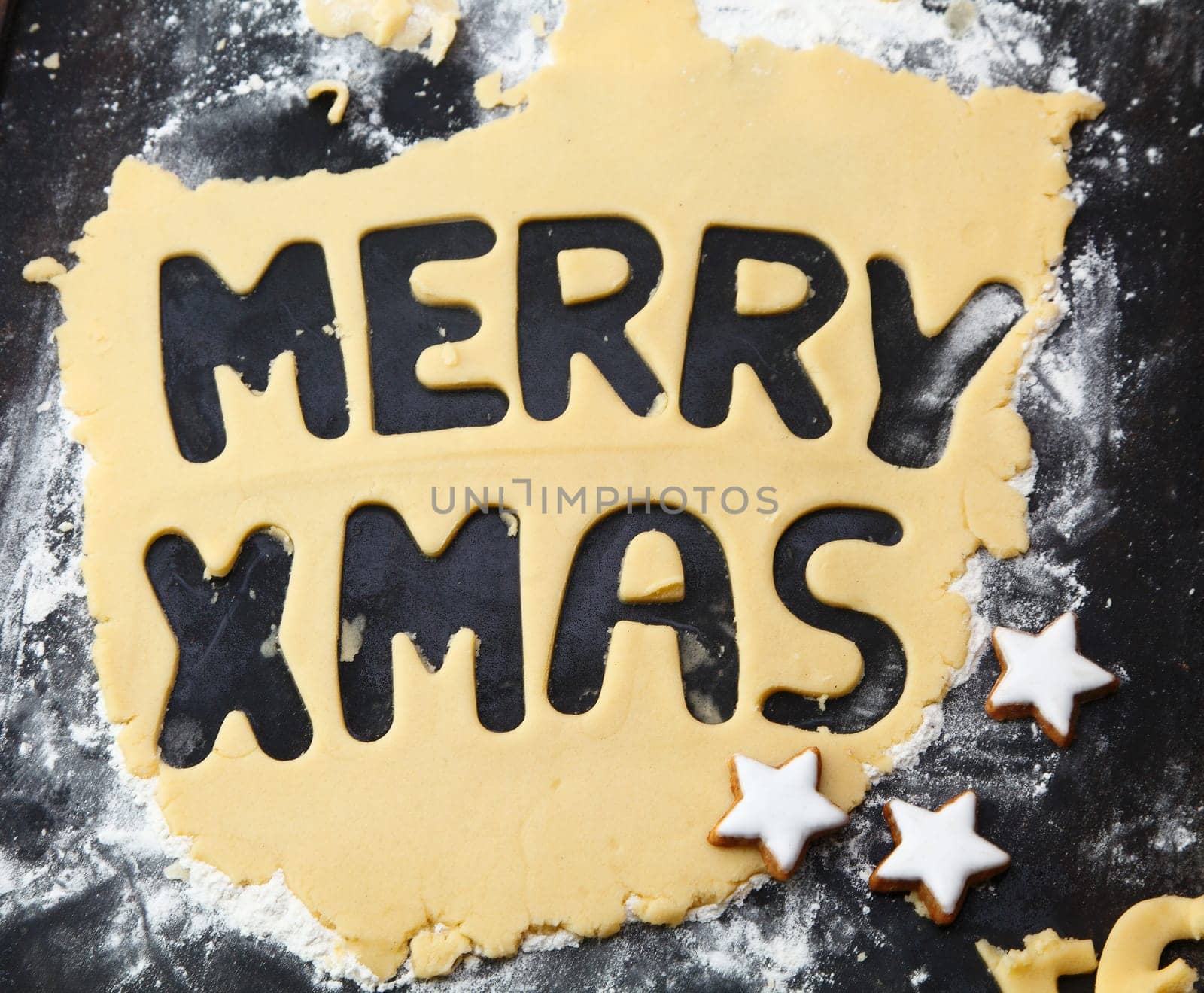 Text Merry Christmas cut out in rolled dough on a floury surface with star biscuits for fun Christmas baking