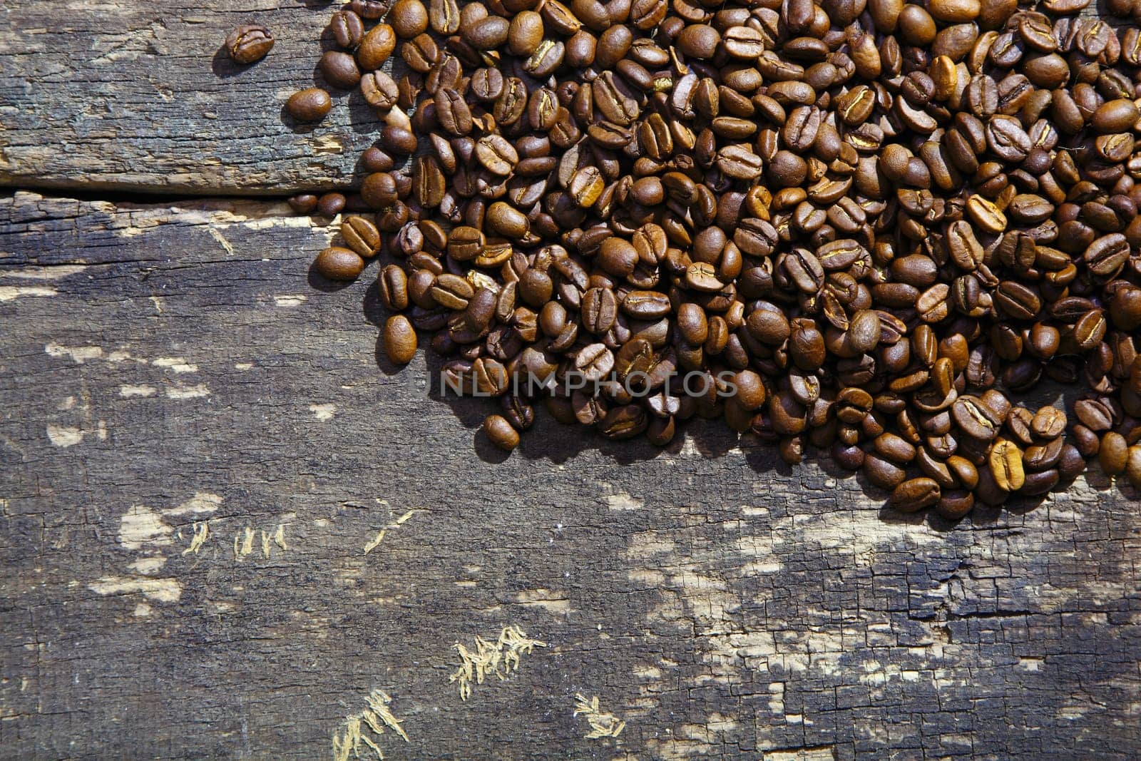 Pile of rich brown freshly roasted aromatic coffee beans on an old grunge wooden surface with copyspace