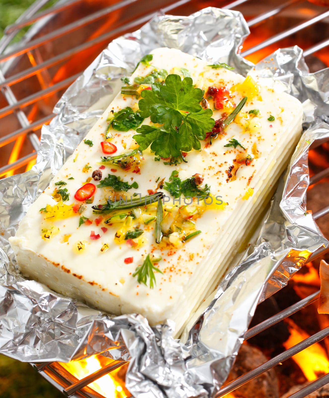 High angle view of a portion of feta or halloumi cheese topped with seasoning and spices grilling on a barbecue