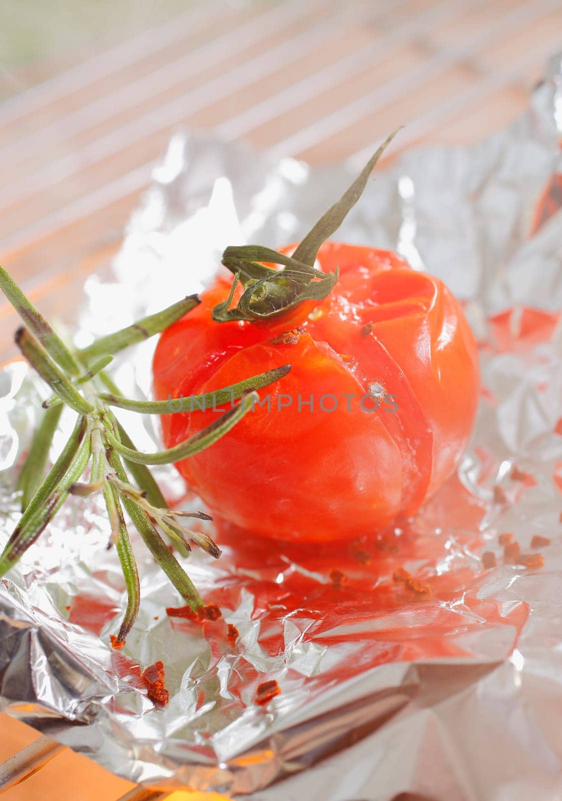 Grilled tomato and sprig of rosemary on aluminium foil