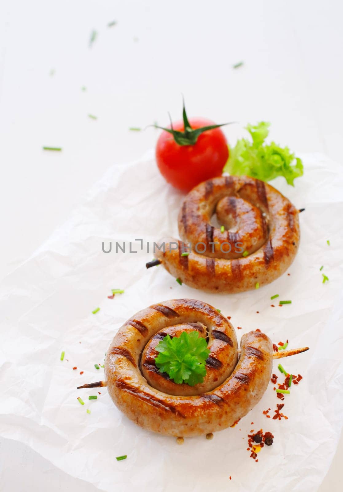 Rolled Bratwurst with tomato on stick over the white background