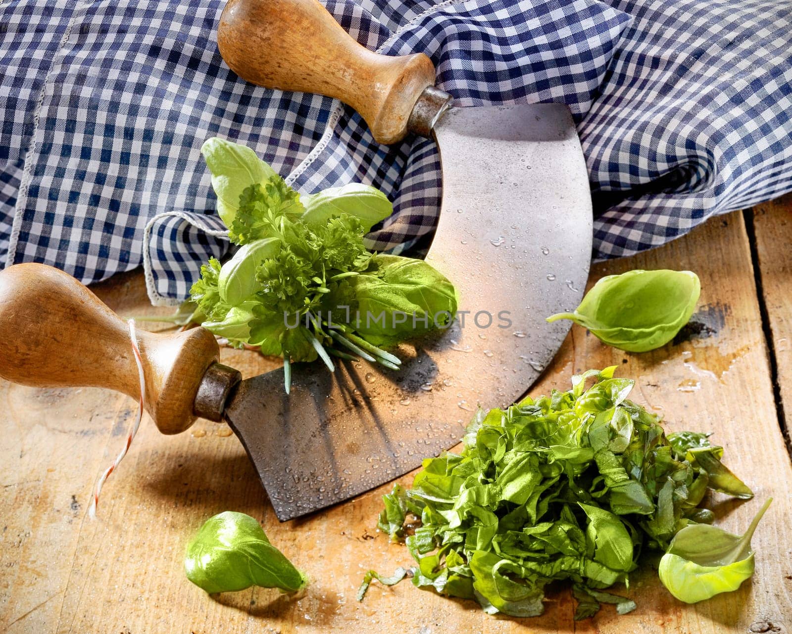 Chopping a selection of mixed herbs in a bunch including basil, parsley and chives using a two handled curved rocker blade on a wooden tabletop