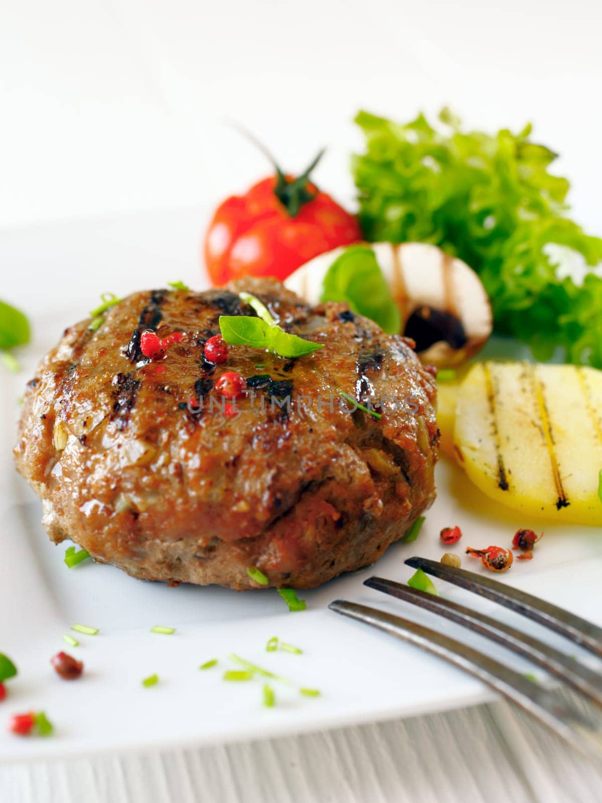 Succulent cooked beef burger with potatoe and salad on a white plate.