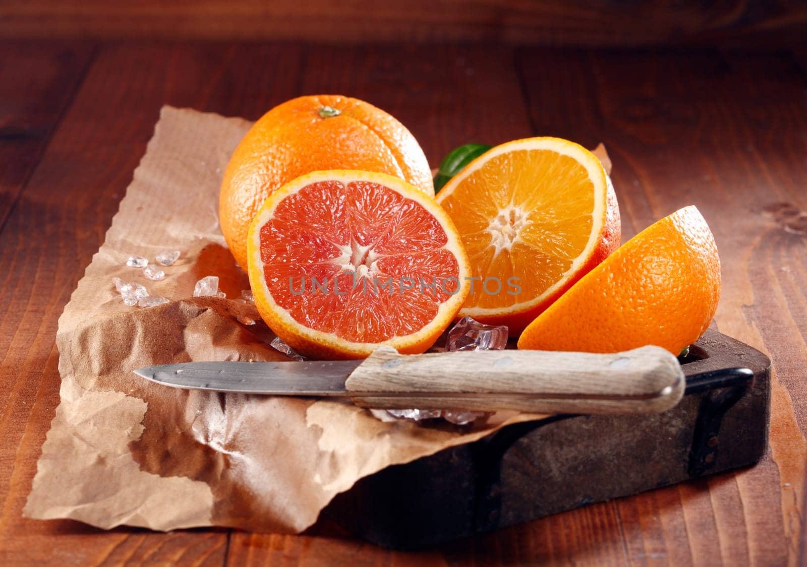 Juicy oranges, one whole and some sliced in halves on brown paper with knife