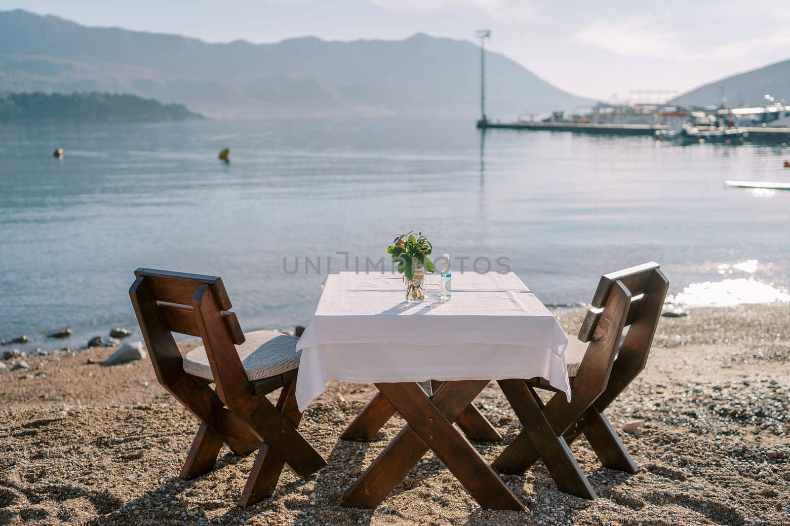 Laid table for two with chairs stands on a sandy beach by the sea by Nadtochiy