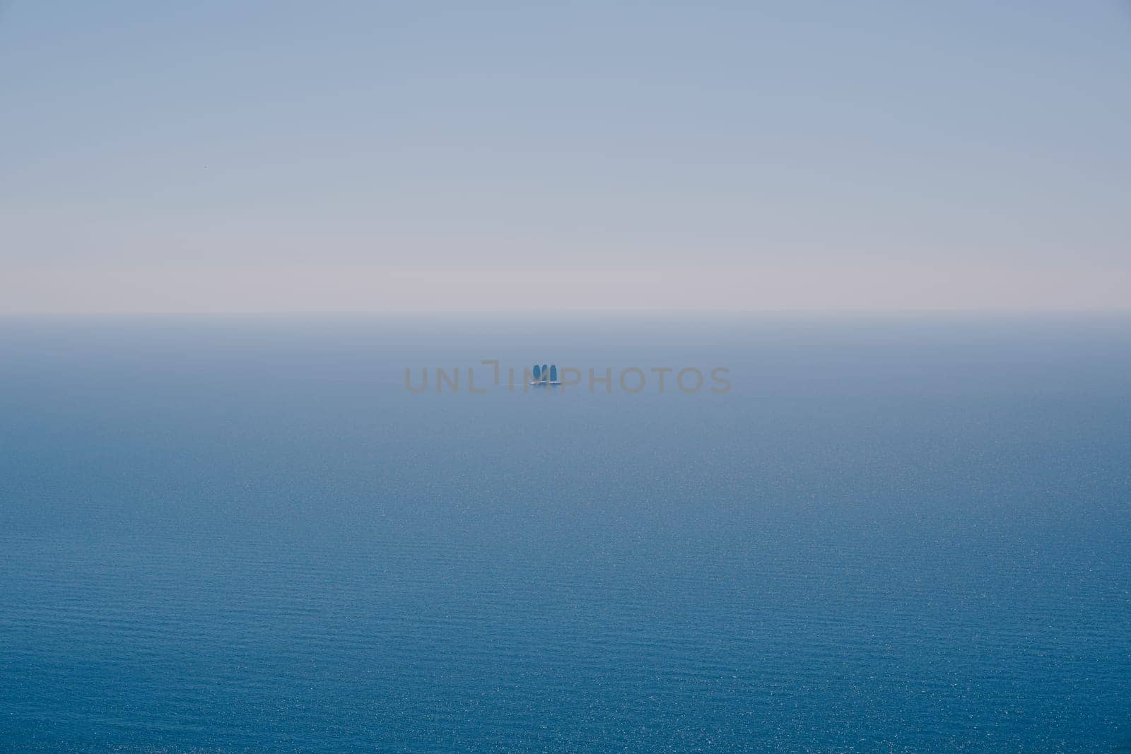 Yacht with three sails floats on the blue sea on the horizon. High quality photo