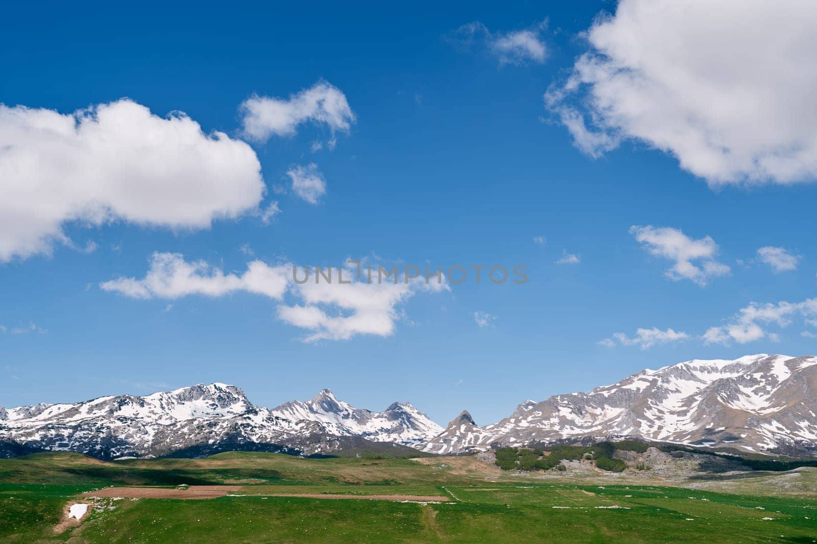 High snow-capped mountain range over sunny green valley. High quality photo