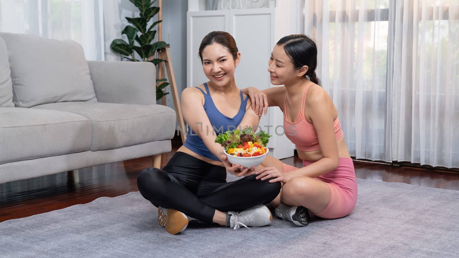 Young sporty Asian women in sportswear holding salad bowl together fill with vibrant of fruit and vegetable. Natural youthful and fit body lifestyle with balance nutrition and home exercise. Vigorous