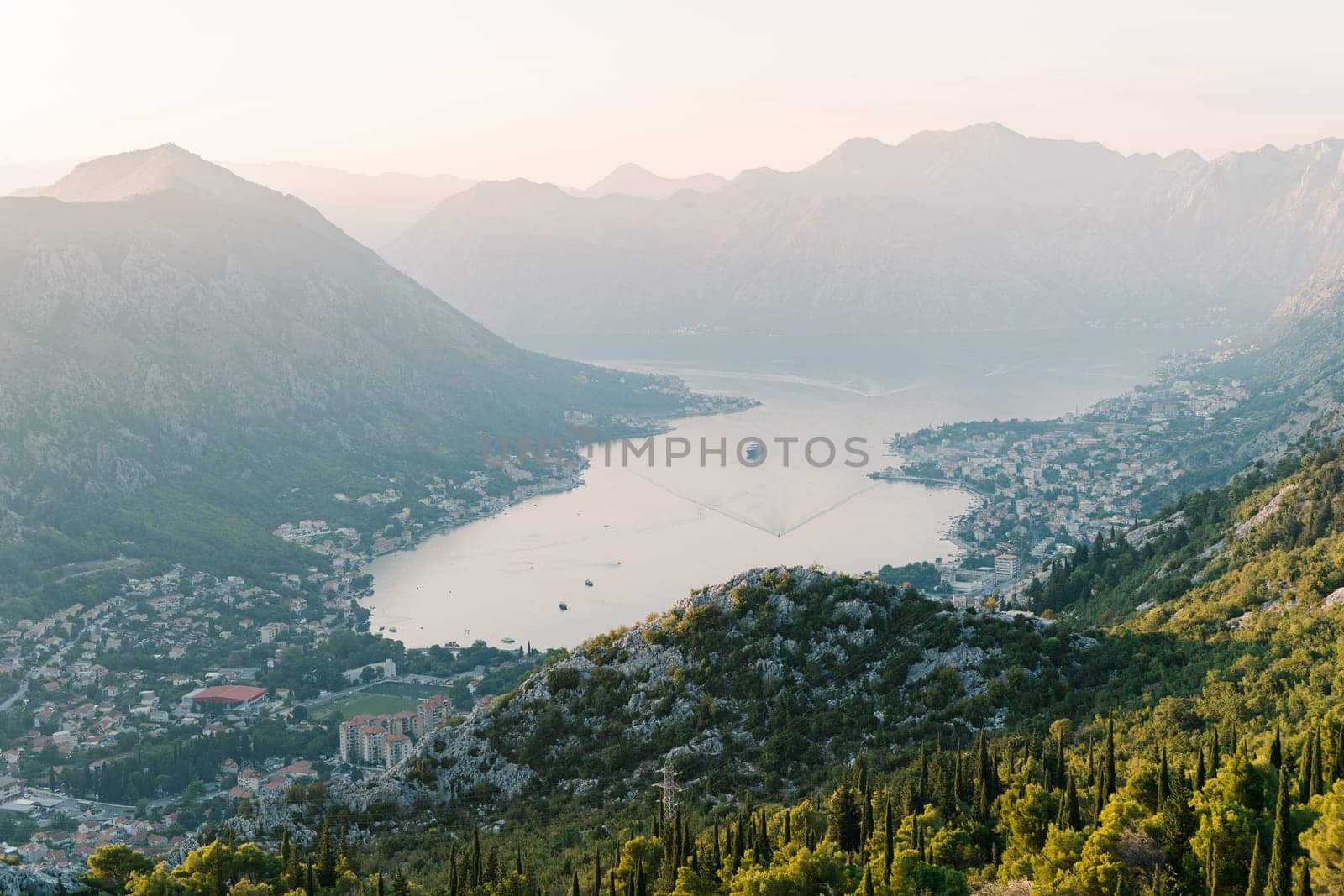 Passenger liner sails along the Bay of Kotor against the backdrop of mountains in the haze. Montenegro by Nadtochiy