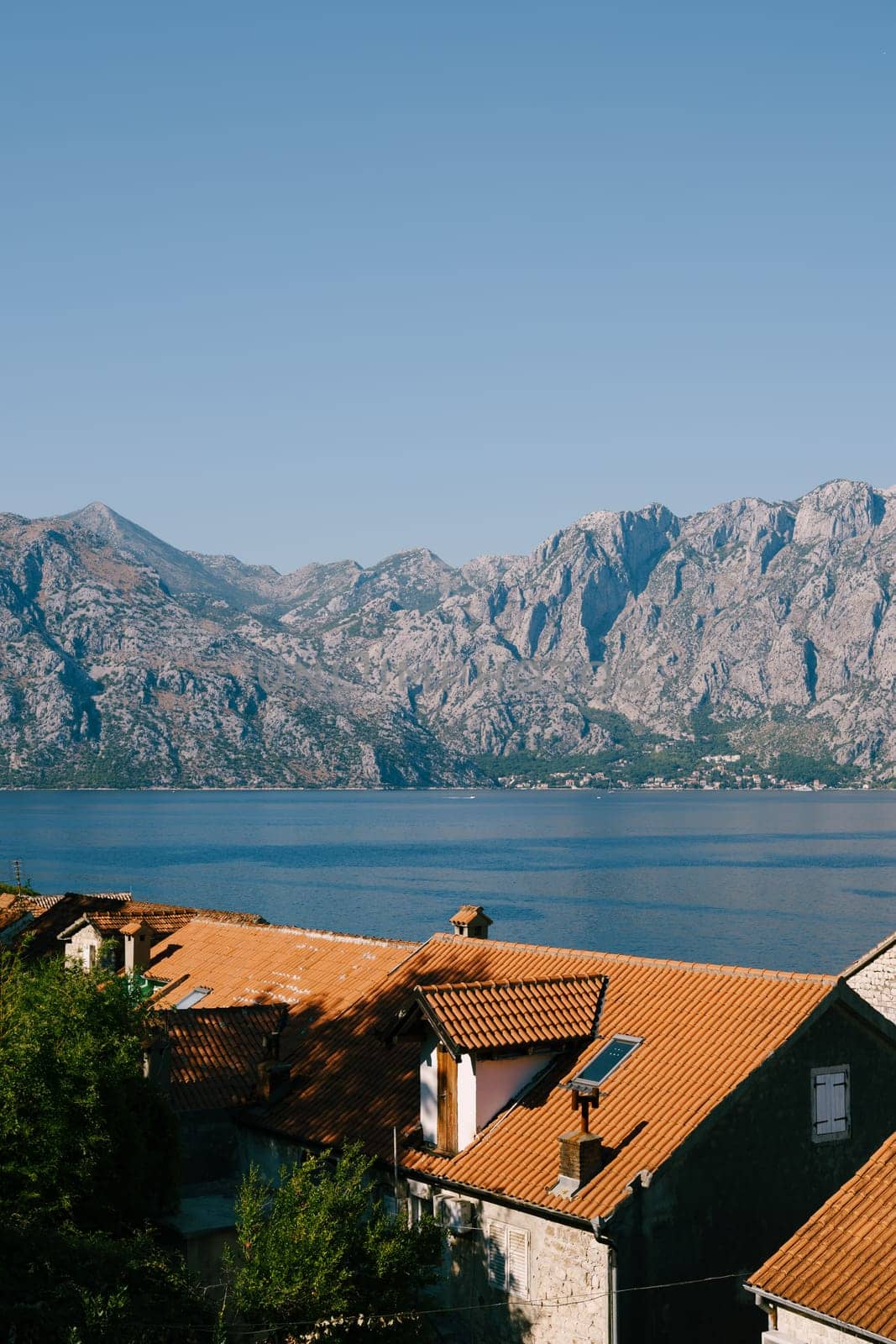 Old houses with red tiled roofs on the seashore near a high mountain range. High quality photo