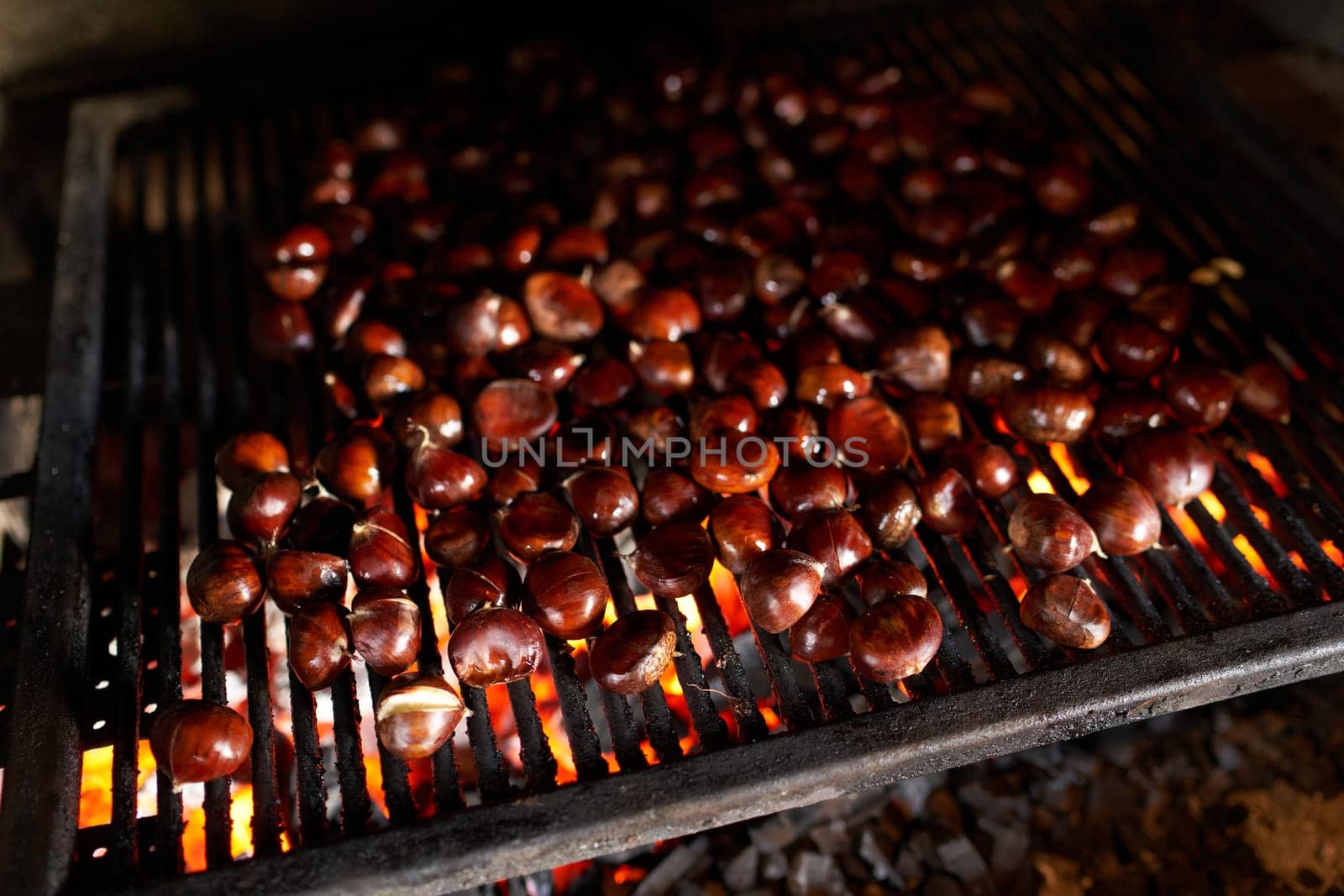 Fresh brown chestnuts are baked on a grill grate in an oven over a fire. High quality photo