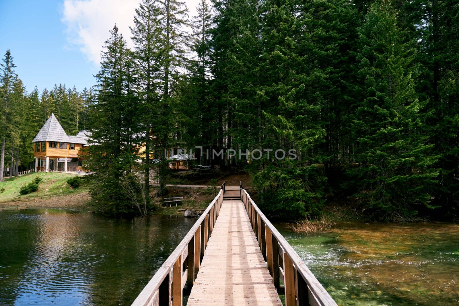 Wooden bridge across the lake to a house on the shore in a spruce forest. High quality photo