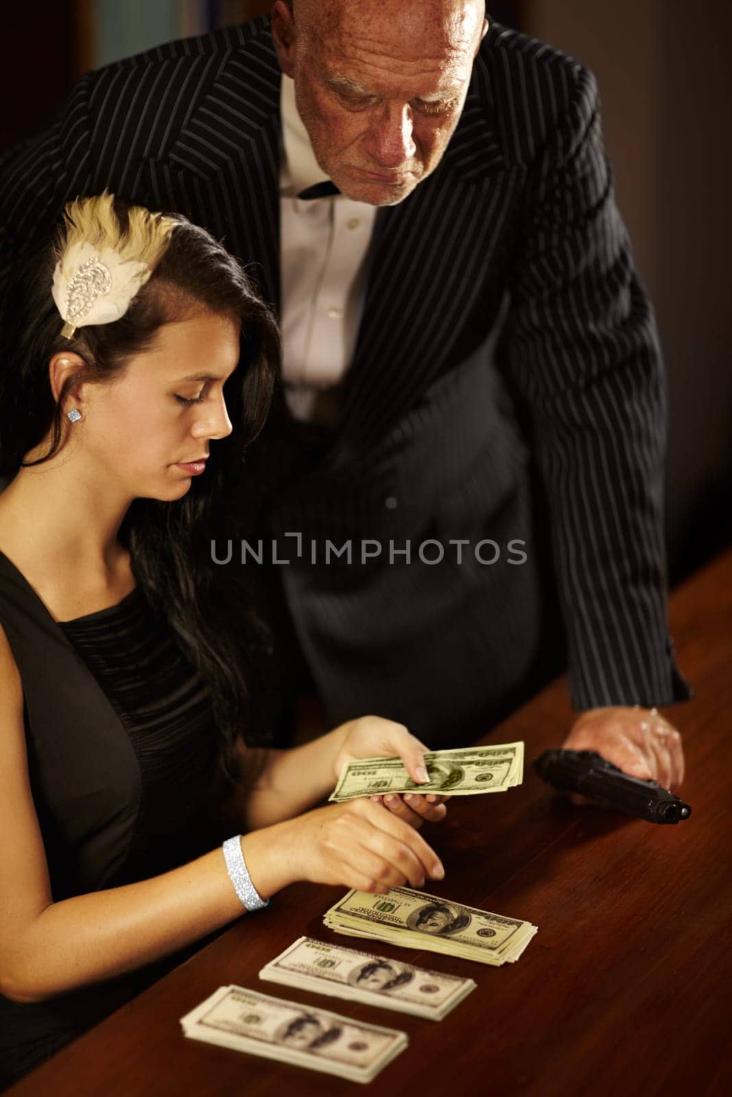 People, count and money with dollar for mafia in office while mob boss, stand and gun for watching. Young woman, retro and fashion with cash on table, desk and checking of fraud in criminal activity.