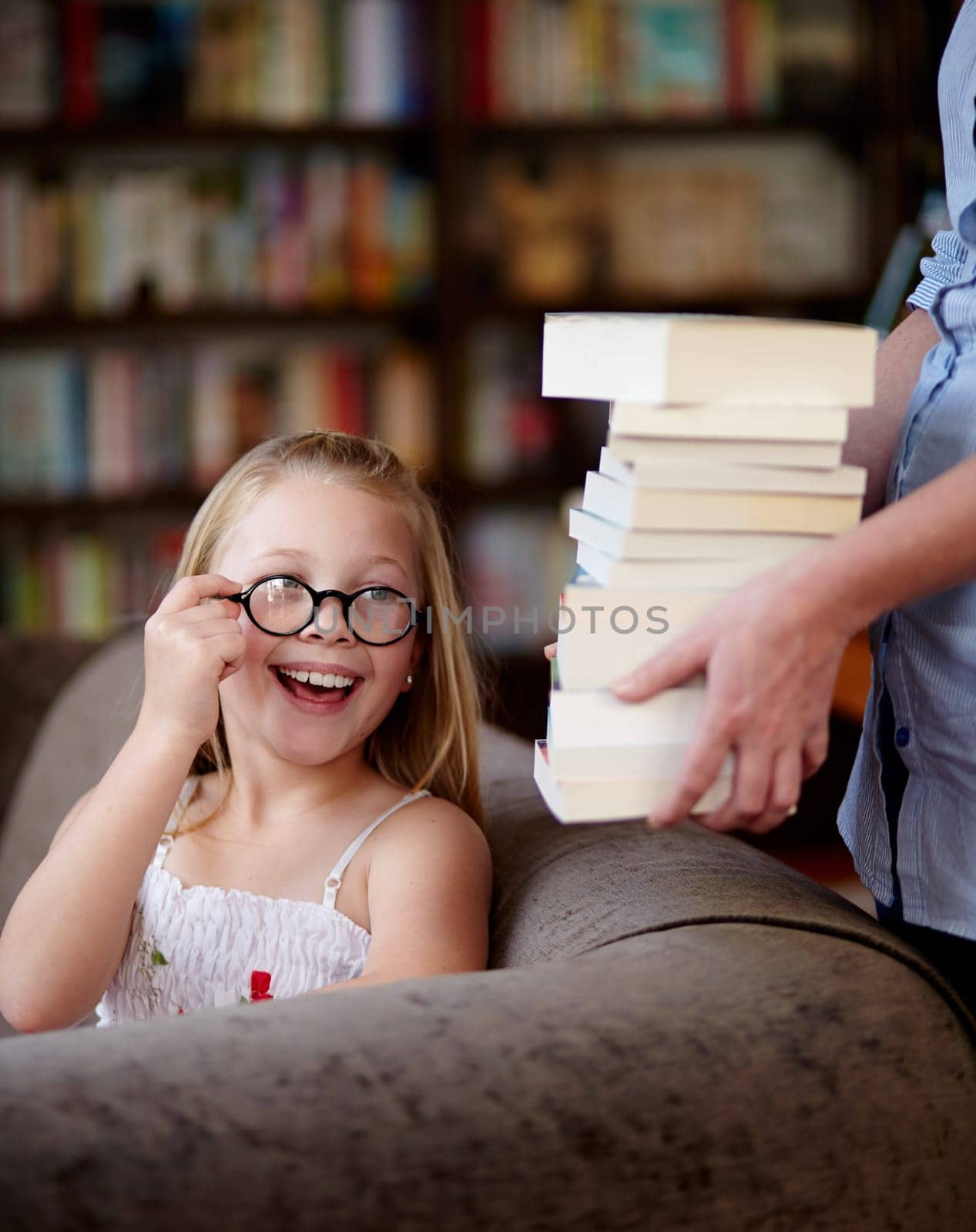 Smile, stack of books and kid in library, learning and relax, studying homework knowledge on couch. School, woman and girl child with glasses in bookstore together with story, and education on sofa. by YuriArcurs