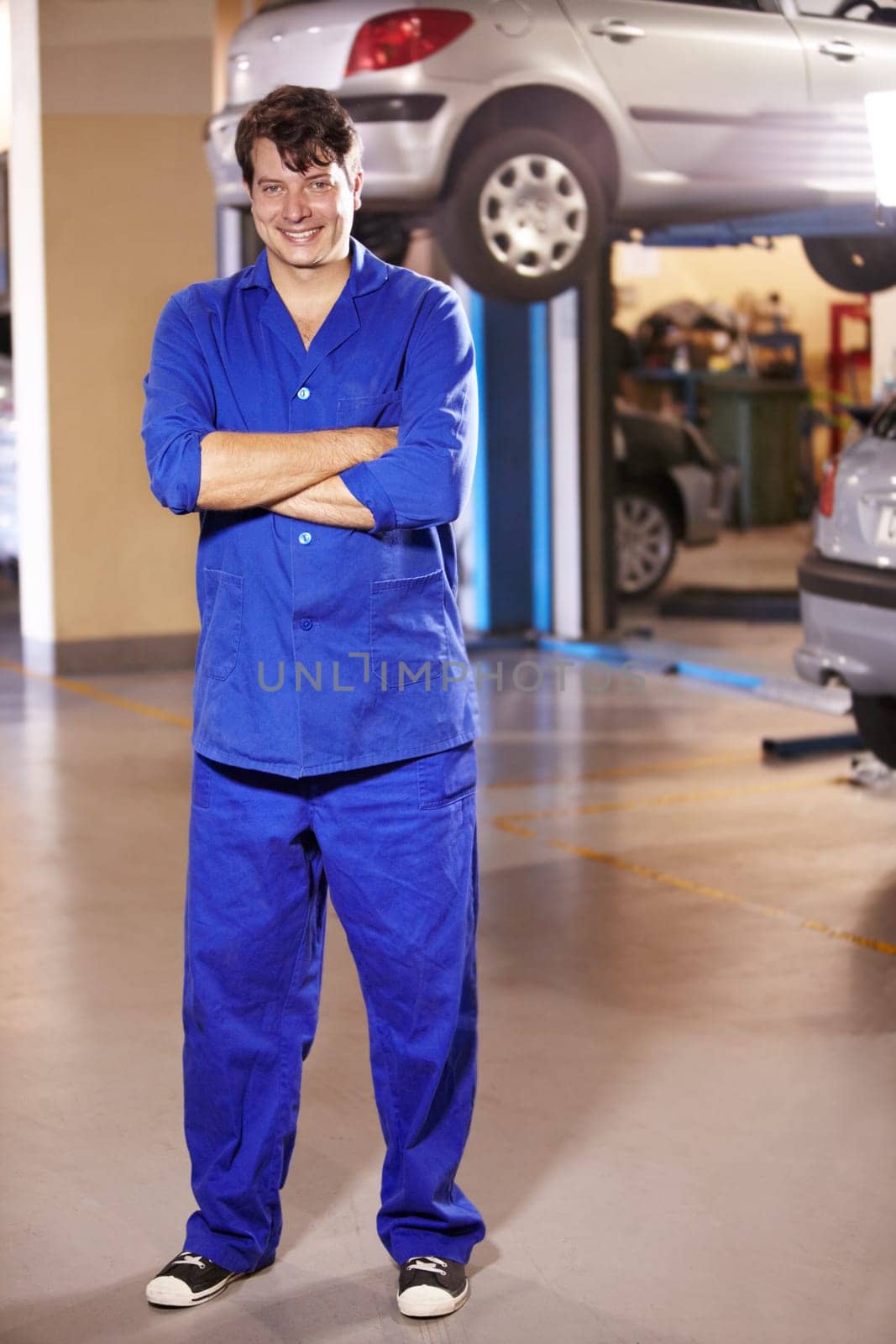 Professional, portrait and mechanic with arms crossed in a workshop for pride in a car. Smile, working and man in a garage for work, maintenance or building a vehicle for transportation or inspection by YuriArcurs