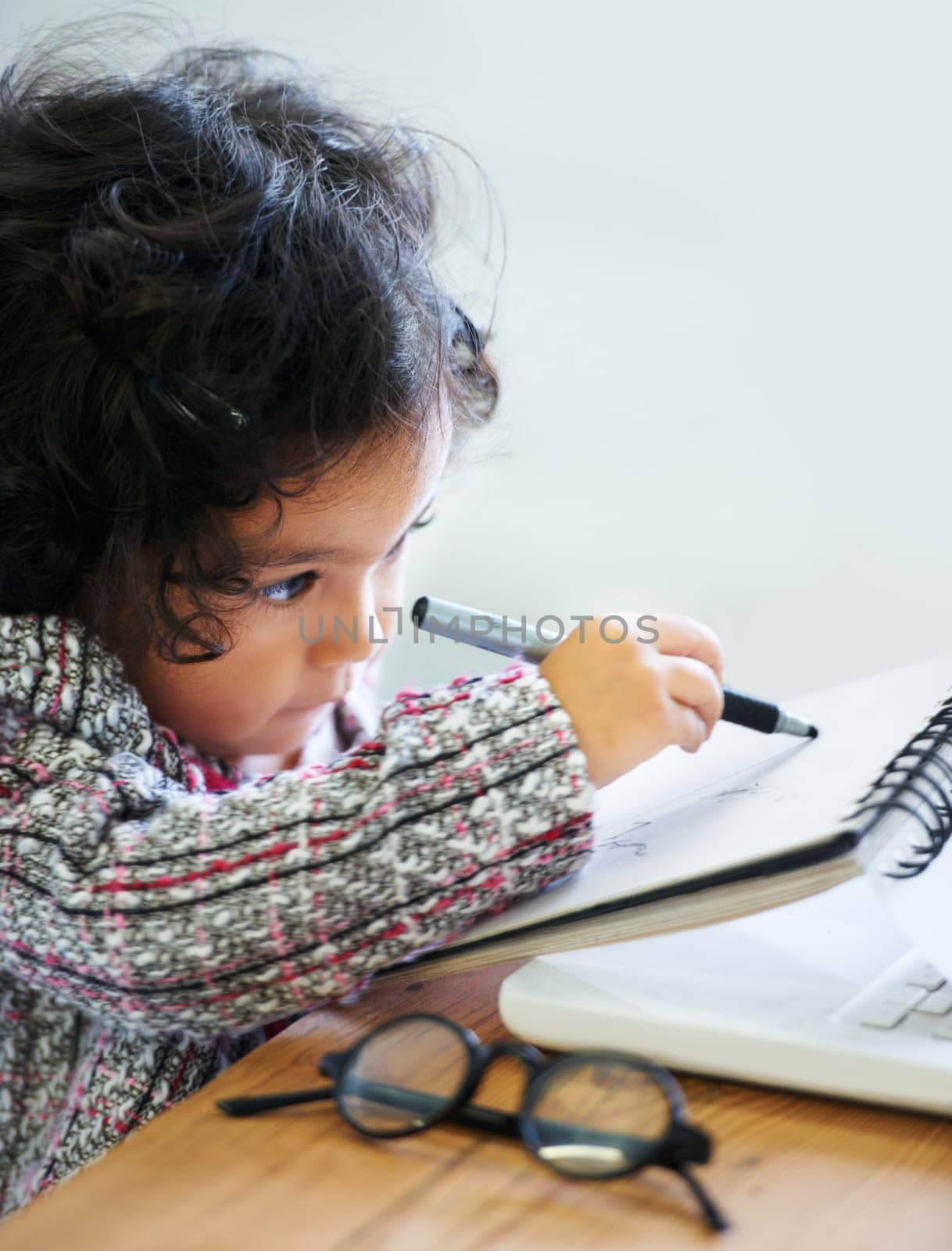 Drawing, art and a child with a book for notes, creativity and learning at a table. House, study and a girl, kid or baby writing in a notebook for education, inspiration or a picture on paper at home.