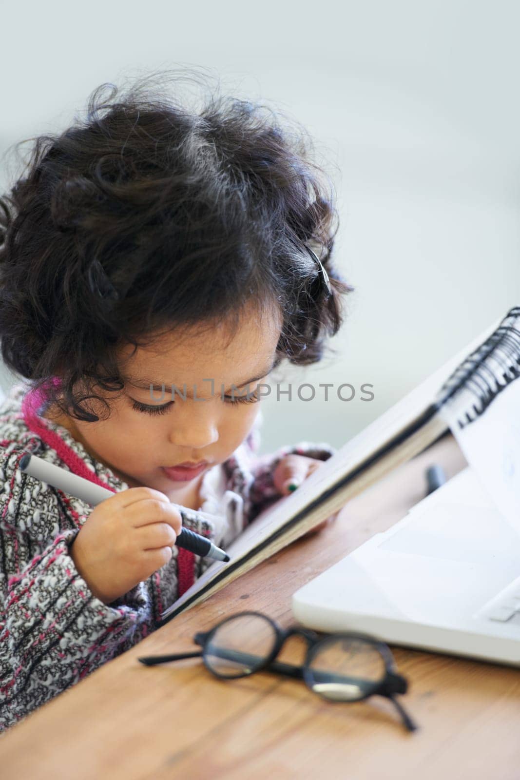 Writing book, learning and a child at a table for education, studying or drawing in a house. Relax, hobby and a girl, kid or baby with a notebook for art, picture or creativity at a home desk.