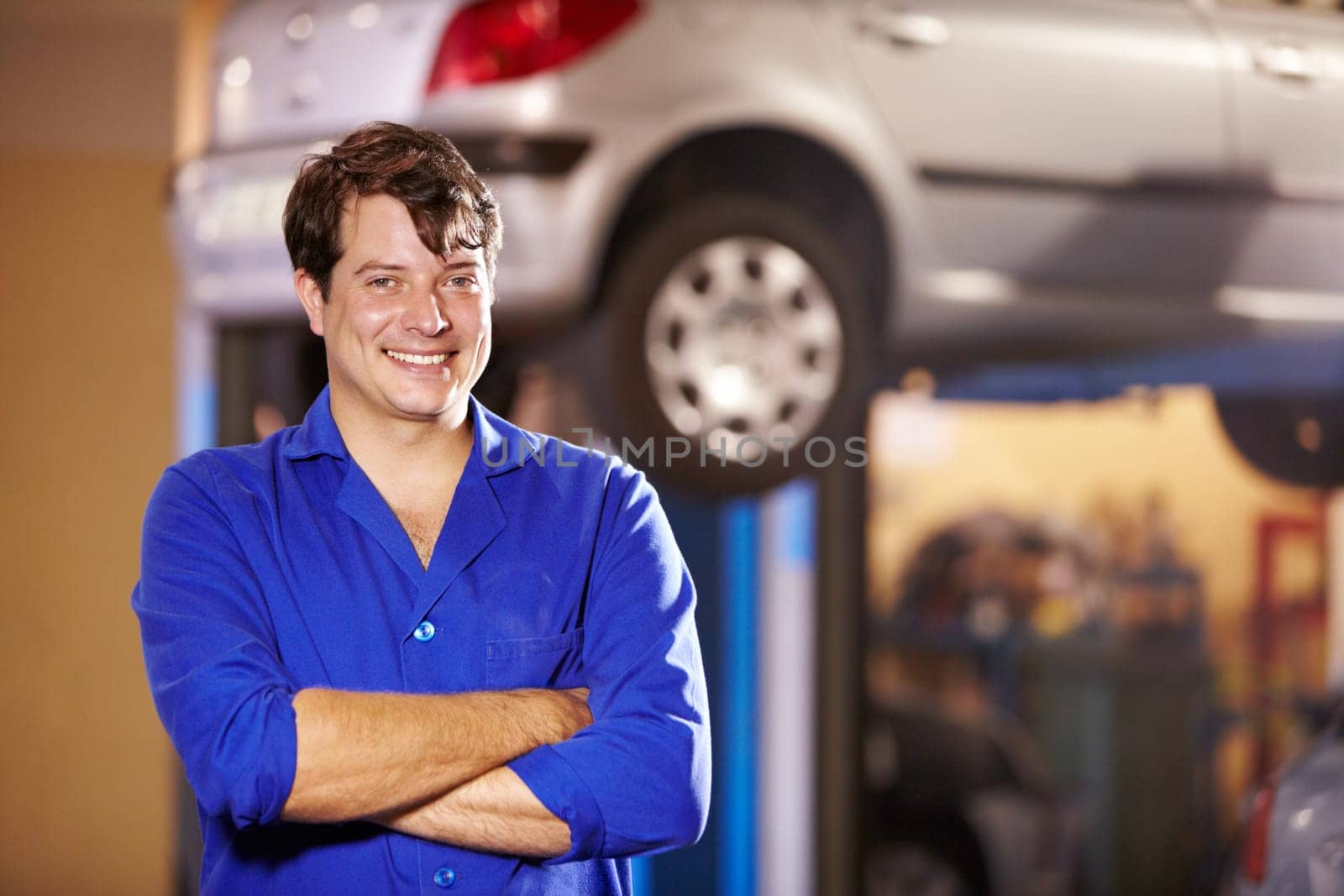 Happy, portrait and a mechanic with arms crossed in a workshop for pride in a car. Smile, working and a man in a garage for work, maintenance or building a vehicle for transportation or inspection.