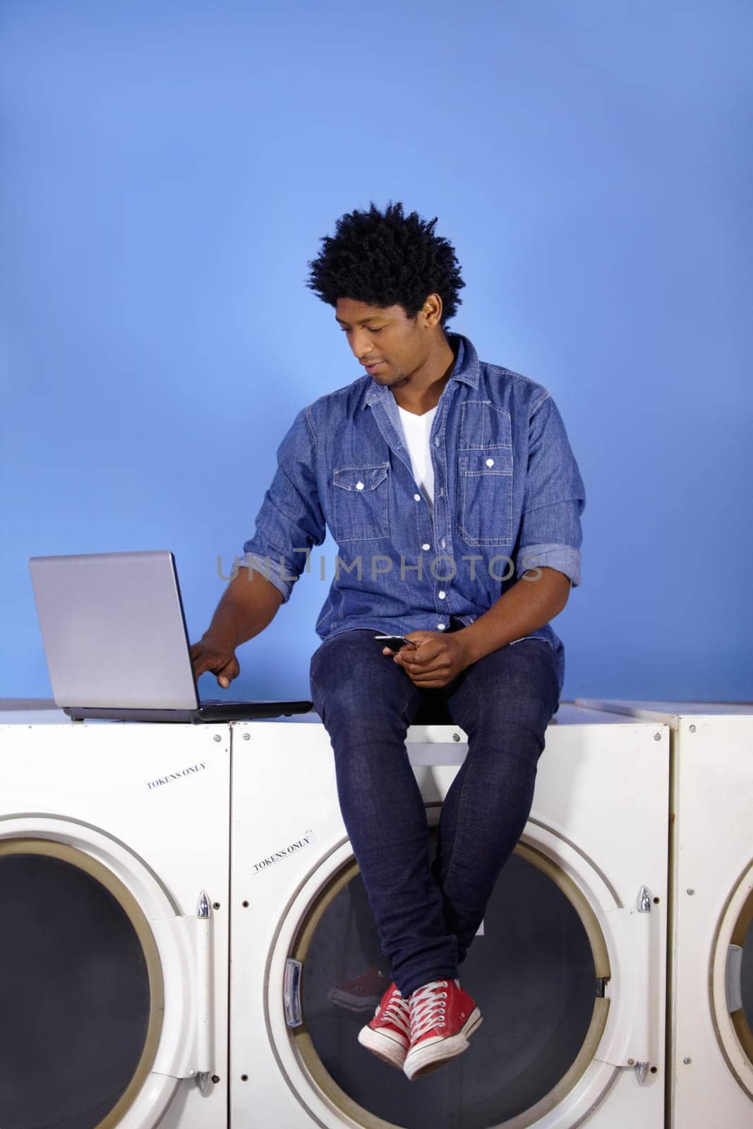 Washing machine, laptop and phone of a black man for laundromat, communication and reading email. Cleaning, typing and a male employee or management of laundry room from the internet with tech.