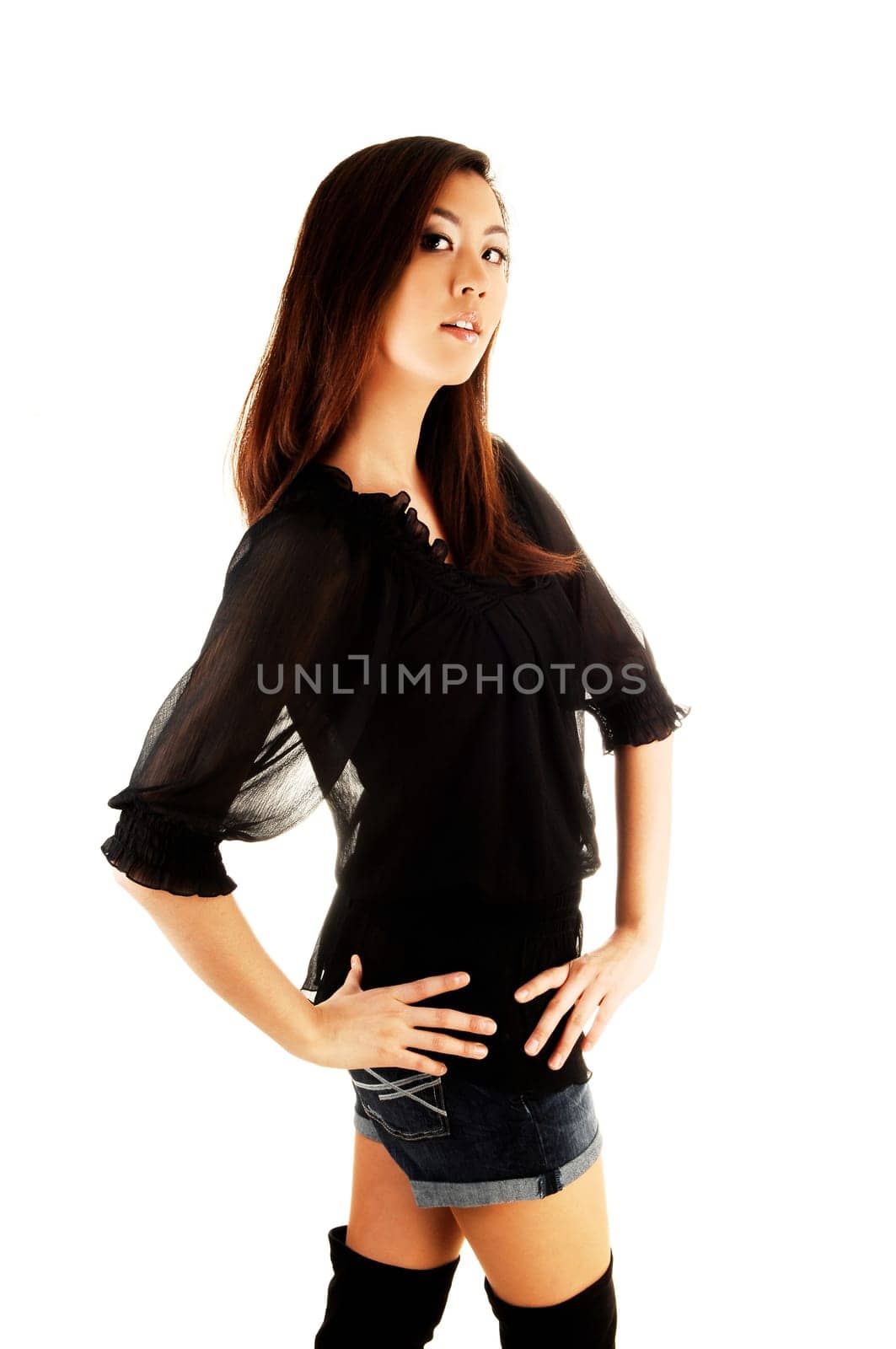 A tall and pretty chinese woman in a black blouse and long black boots standing in the studio for white background.